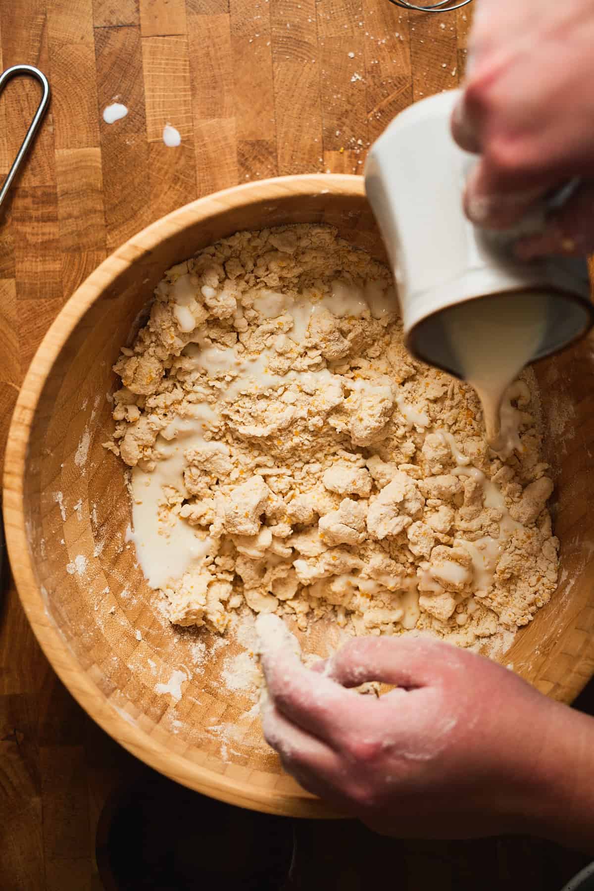 Buttermilk being poured into flour mixture in a wooden bowl.