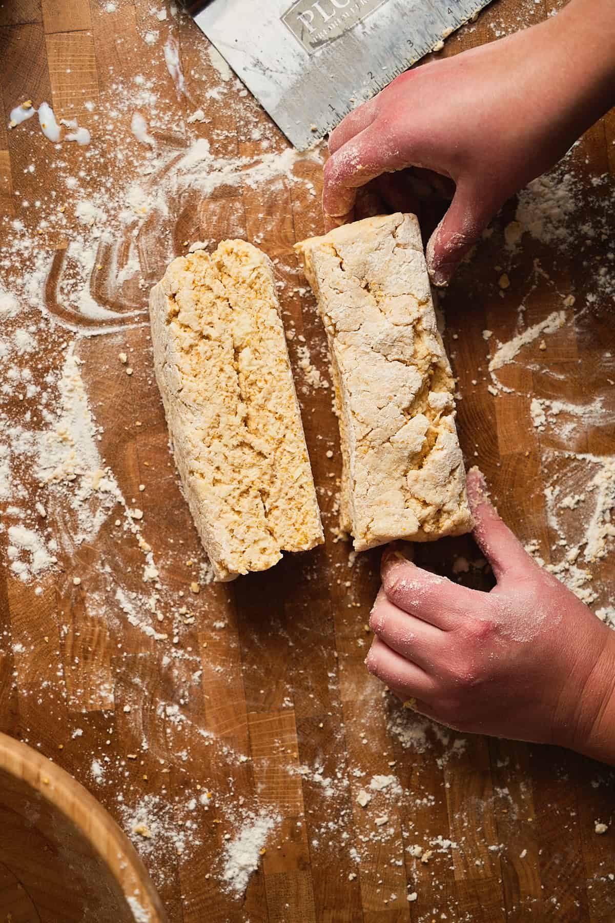 Biscuit dough cut in half to show flaky layers beginning to form on wooden surface with flour and ruler, preparing baking ingredients.