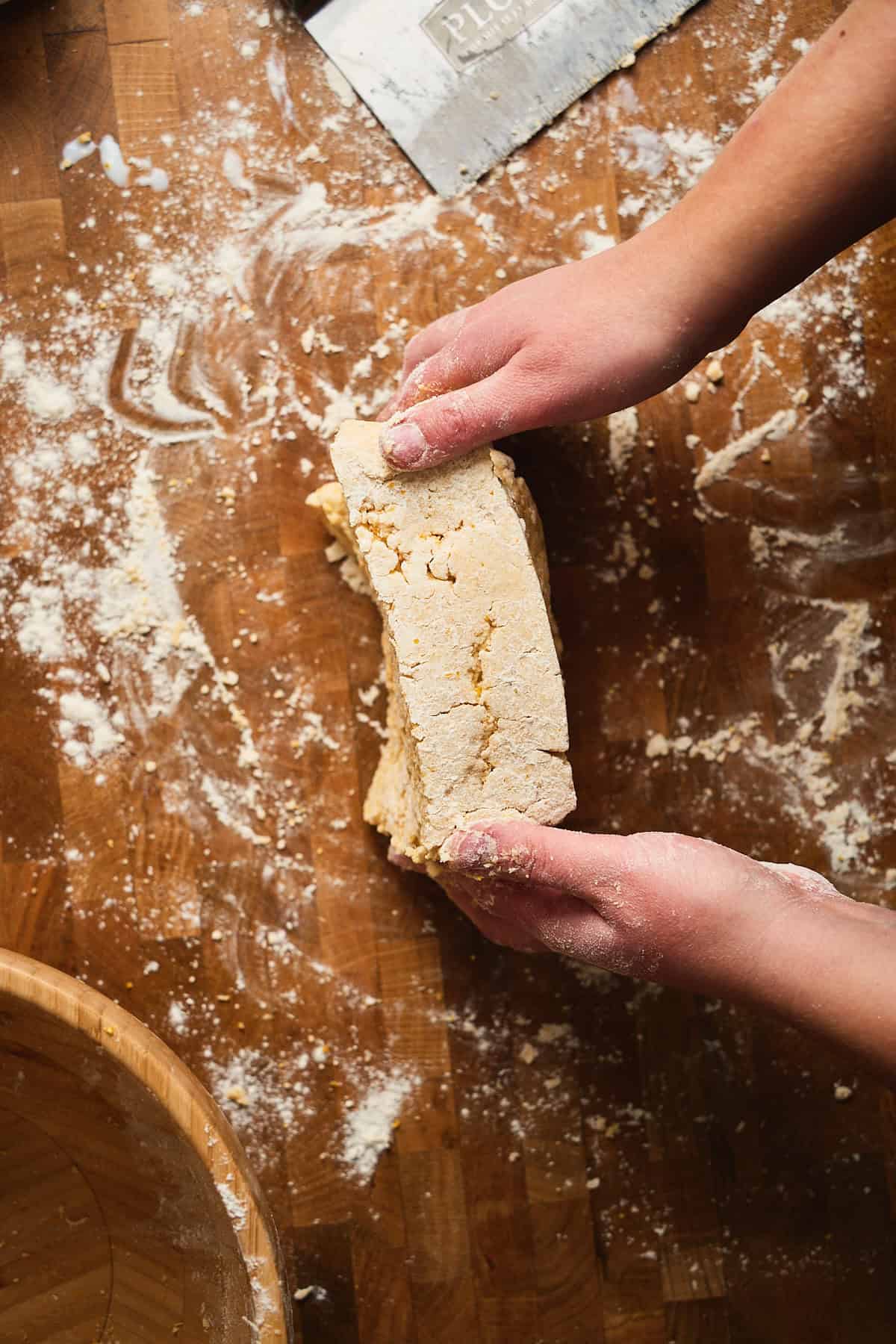 Biscuit dough being stacked on top of eachother to create layers on a wooden surface.