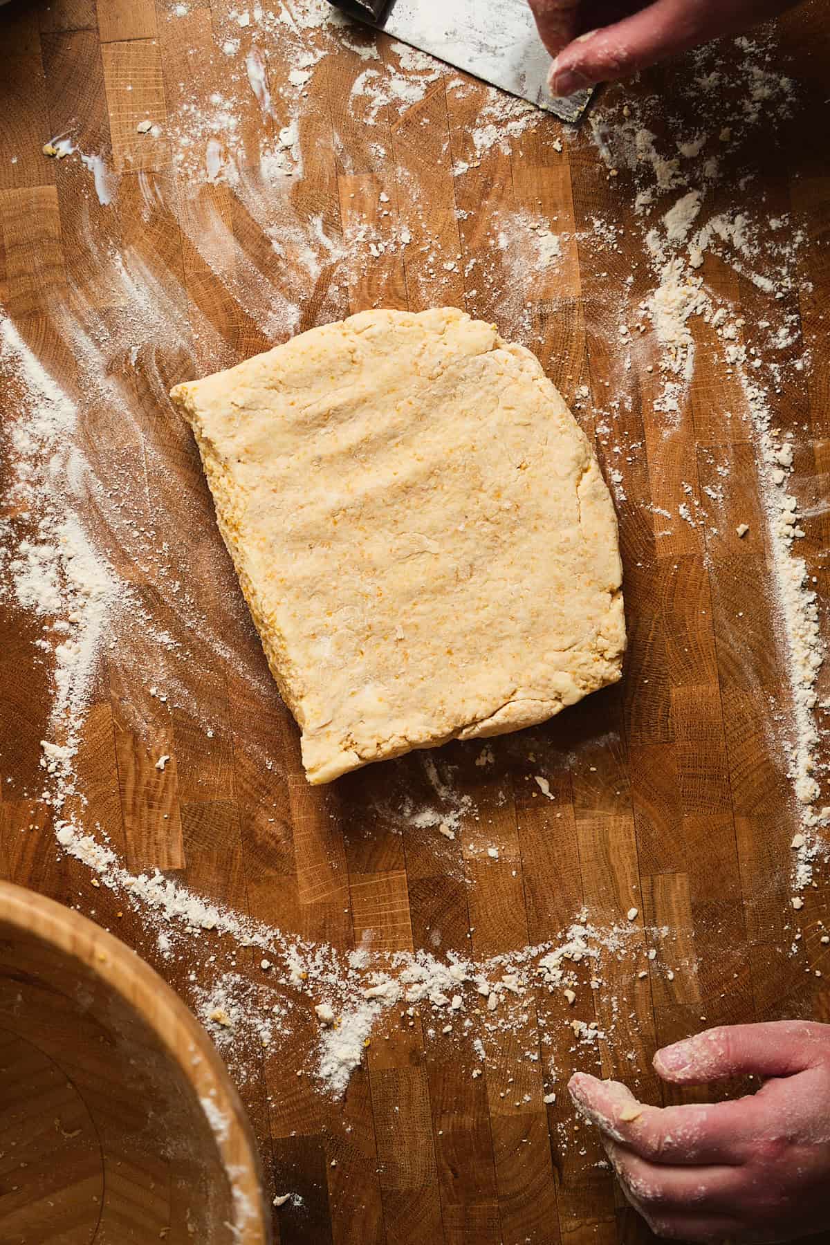 Dough pressed into a rectangle shape on a wooden surface with flour on it.