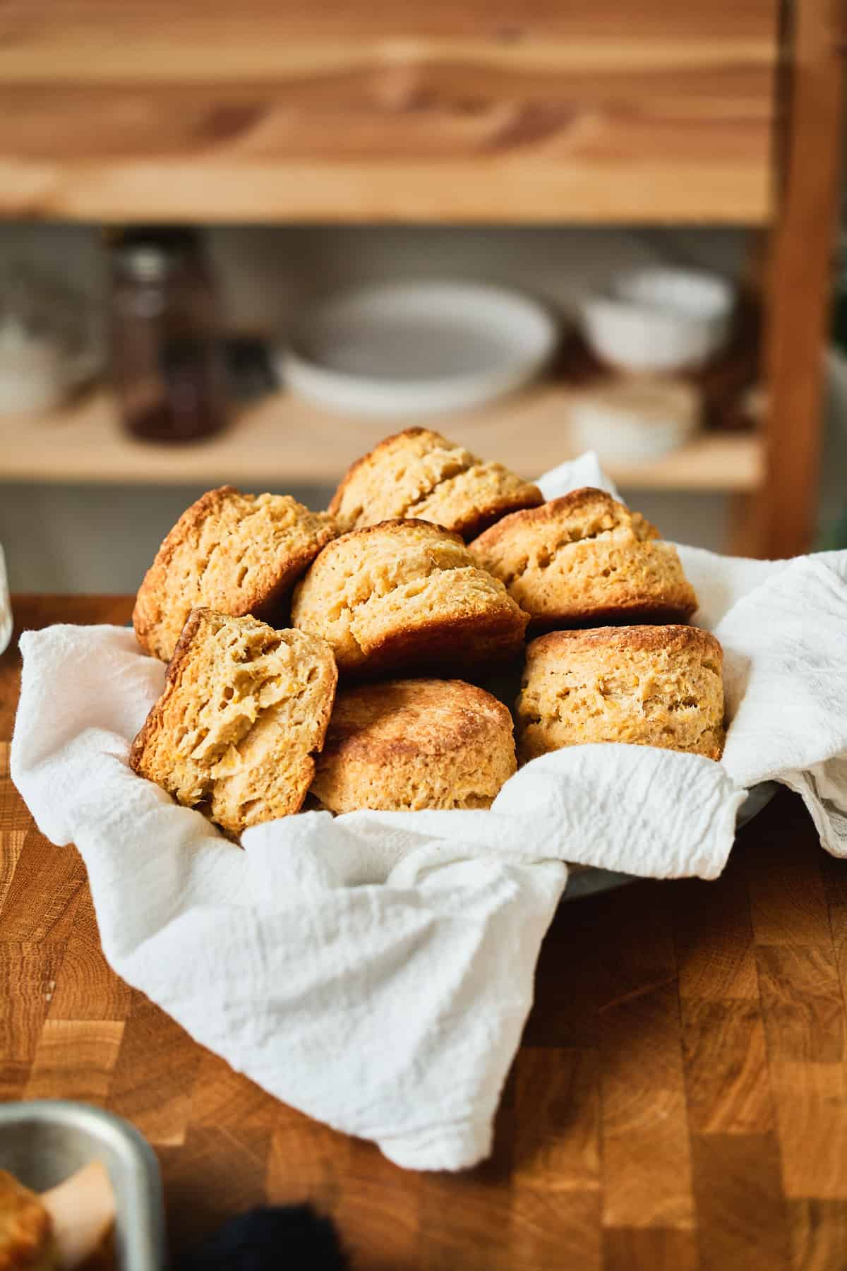 Pile of delicious buttery and flaky cornmeal biscuits in a small metal tin on top of a white linen napkin on a wooden table.
