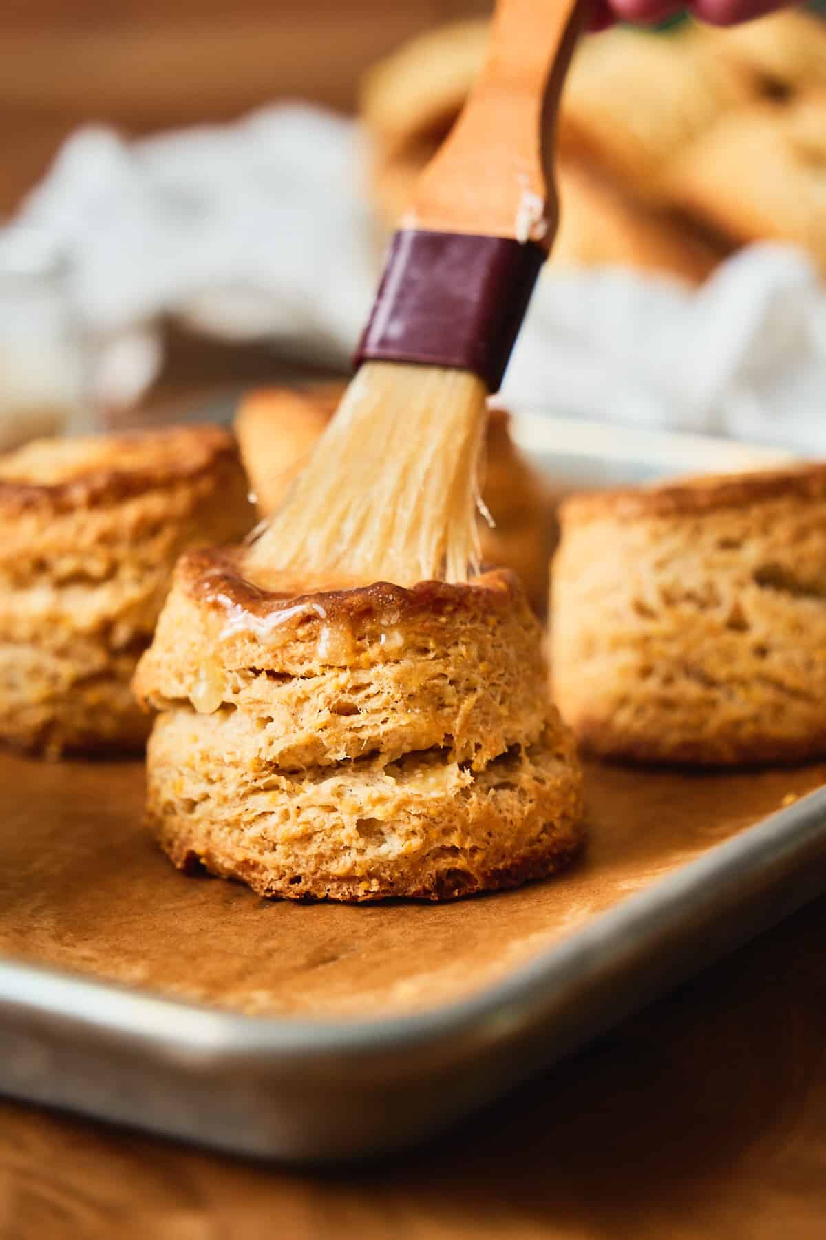 Close-up view of tall, flaky cornbread biscuits with lots of layers, being brushed with honey butter.