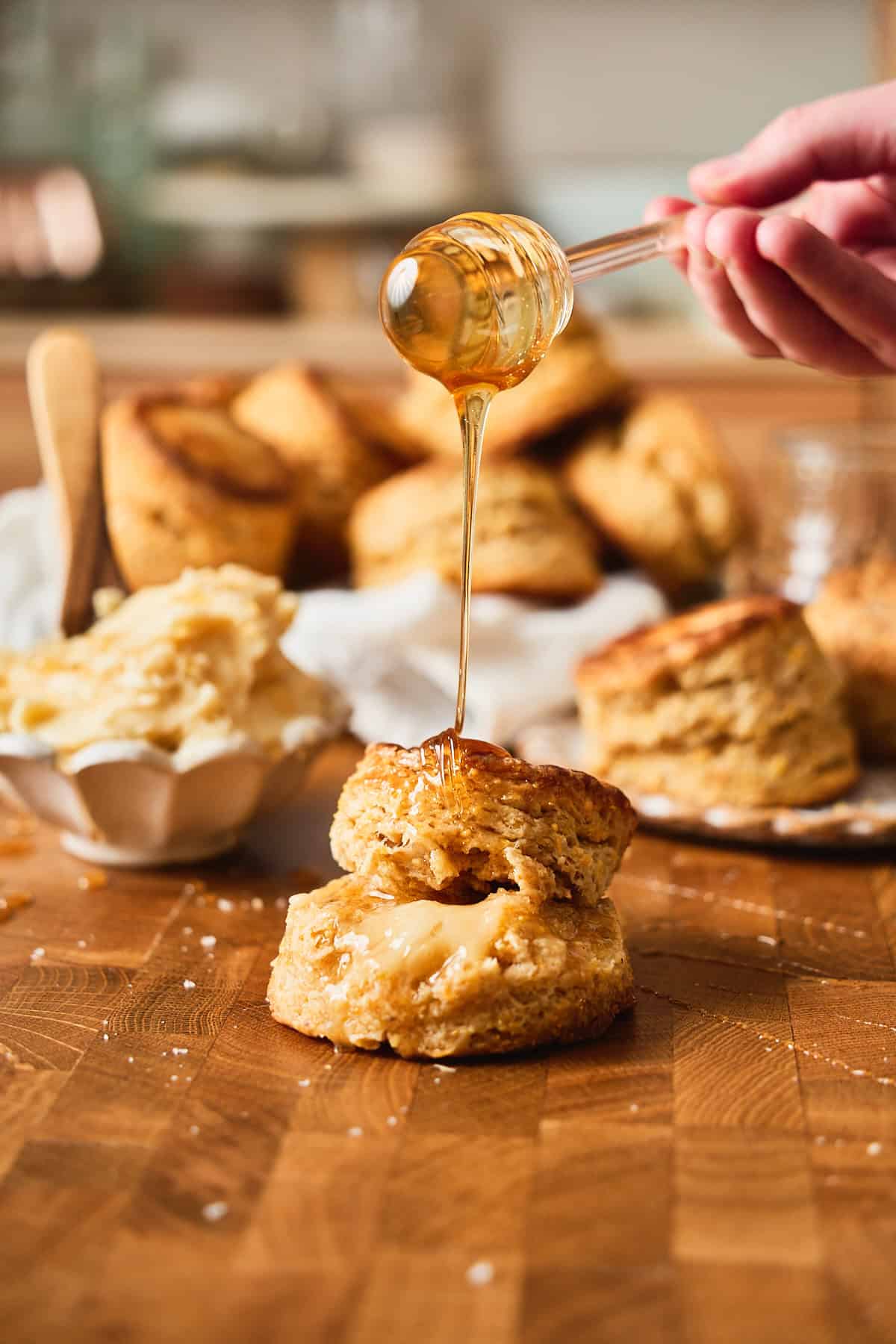 Buttermilk cornbread biscuits drizzled with honey on a wooden surface wit ha stack of biscuits in the background.