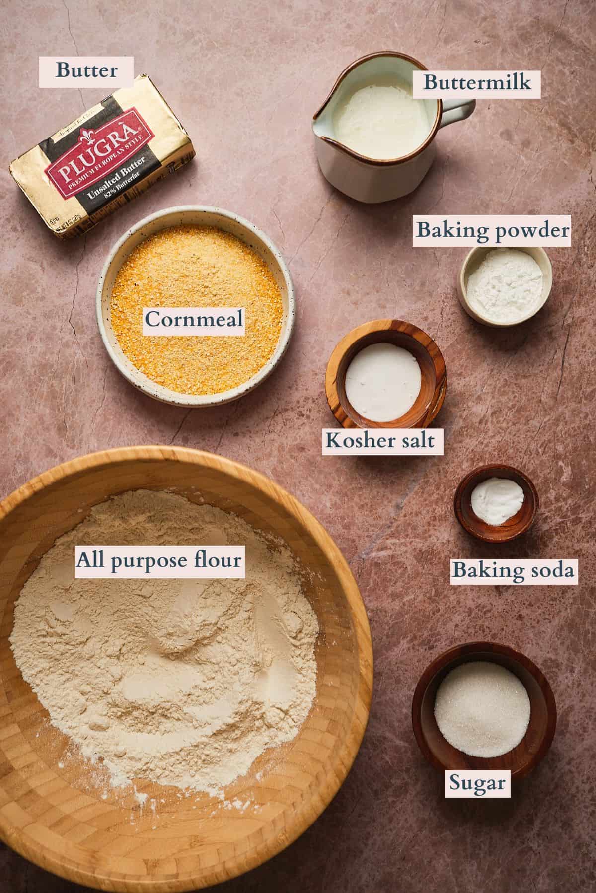 Flour, baking powder, sugar, and ingredients for baking on a brownish pink surface, labeled to denote each ingredient.