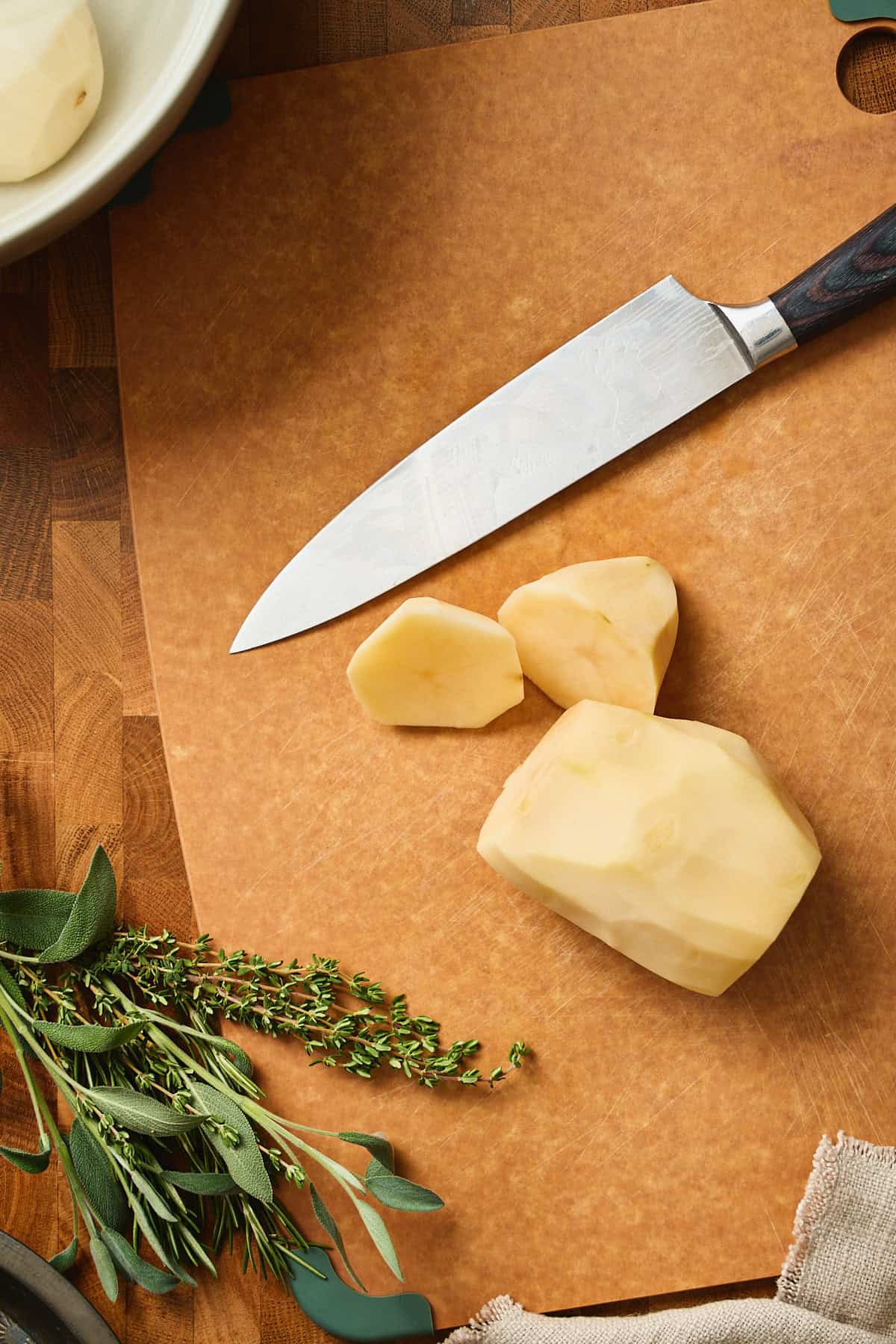Cutting peeled potatoes on cutting board with knife.