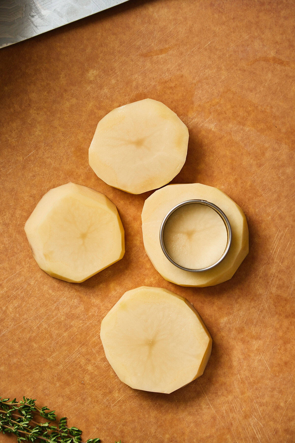 Smooth peeled potatoes with metal cutter on wooden cutting board.