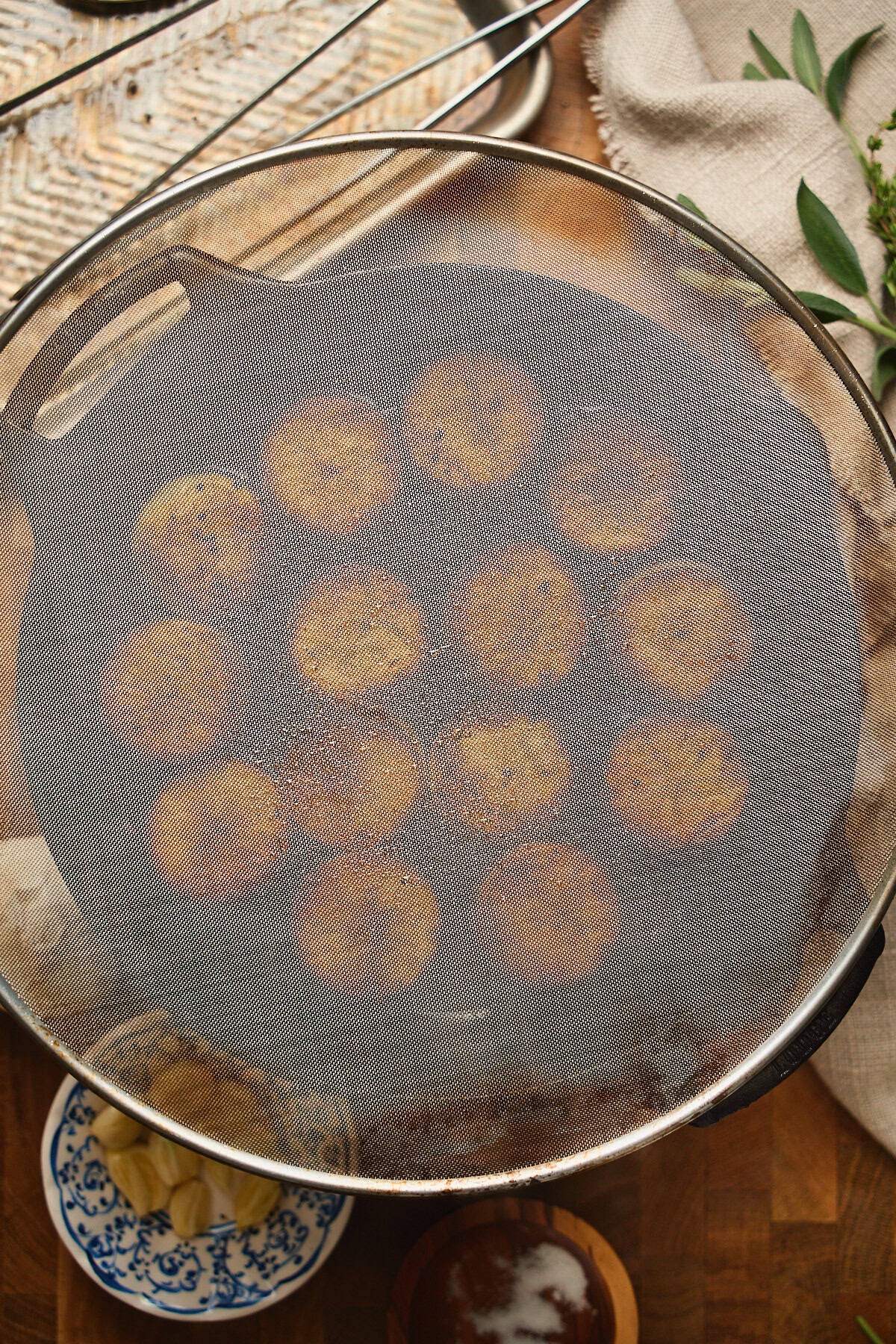 Skillet full of browning potato rounds with a splatter screen overtop.