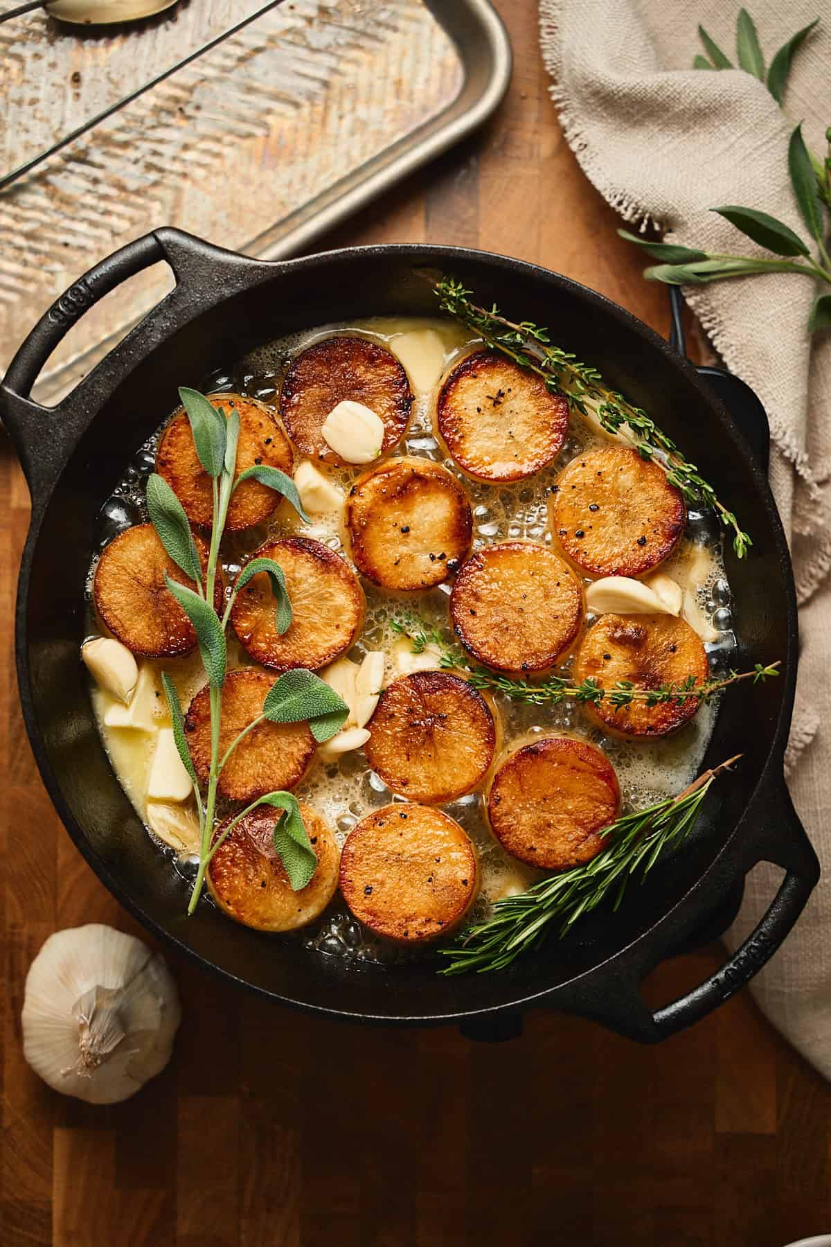 Butter bubbling away in a skillet with fondant potato rounds, herbs, and smashed garlic.