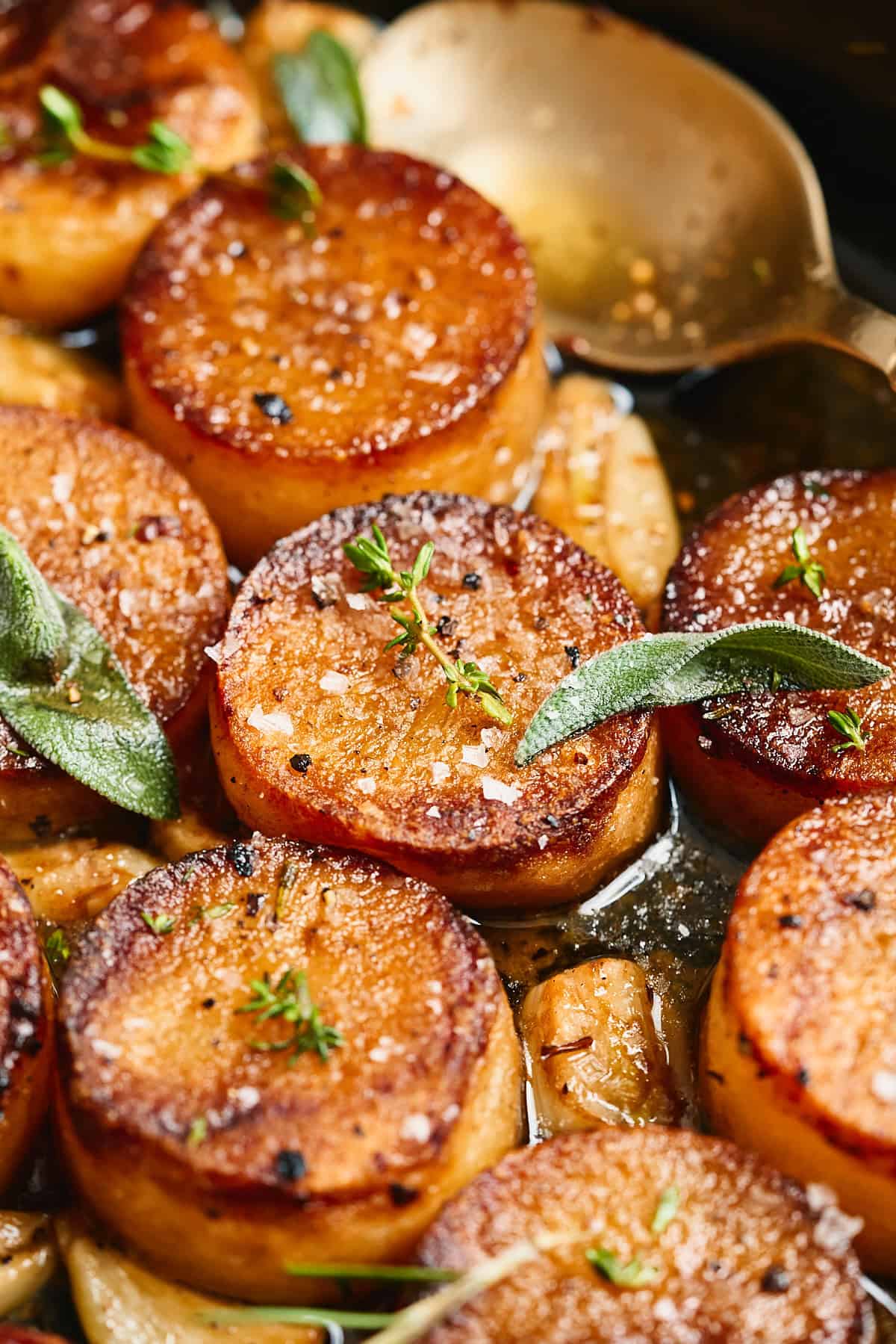 Fondant potatoes topped with herbs and seasoning in a buttery sauce.