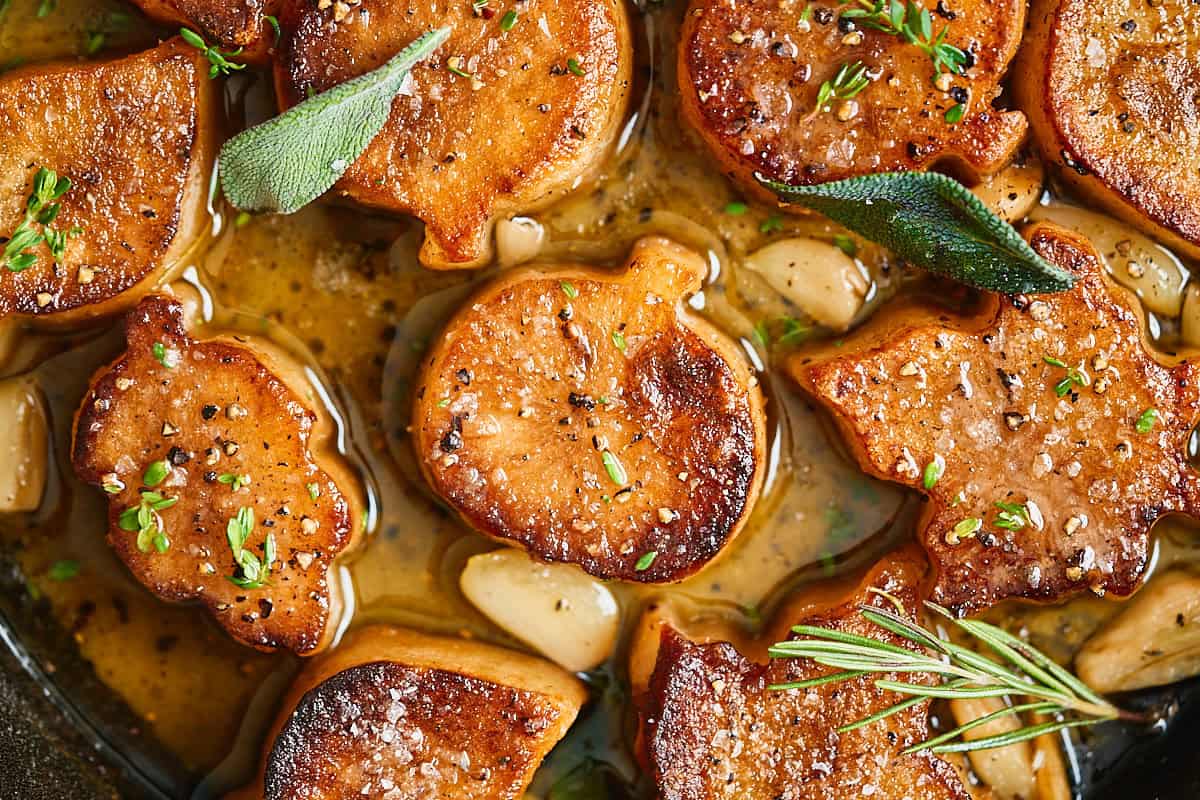Overhead view of melting potatoes shaped like pumpkins and leaves in a buttery white wine sauce with garlic and herbs in a cast iron skillet.