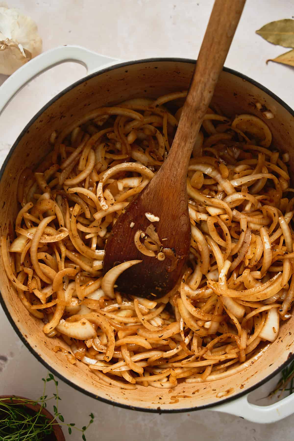 Onions in a pot with a wooden spoon stirring them after they have started to cook down a bit.