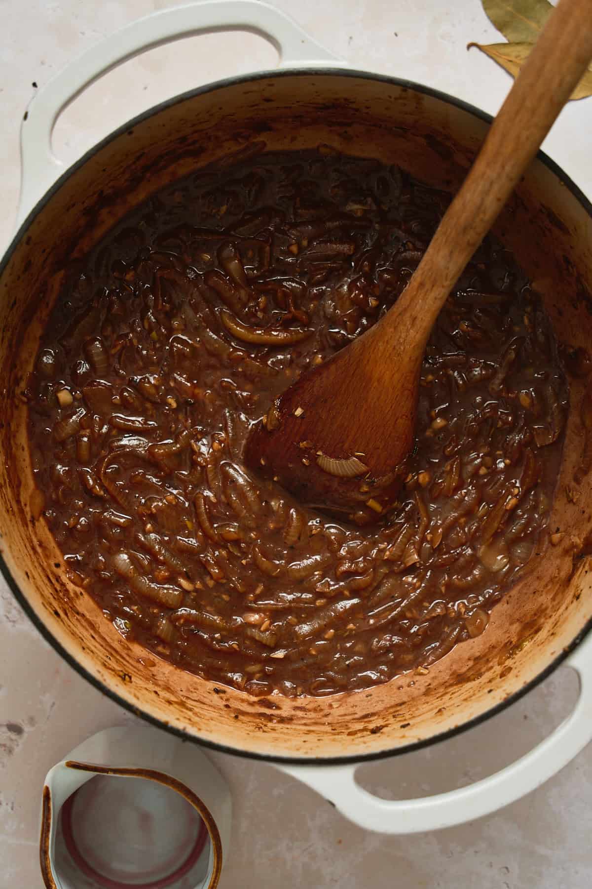 Red wine added to caramelized onions in a Dutch oven with a wooden spoon in the pot.