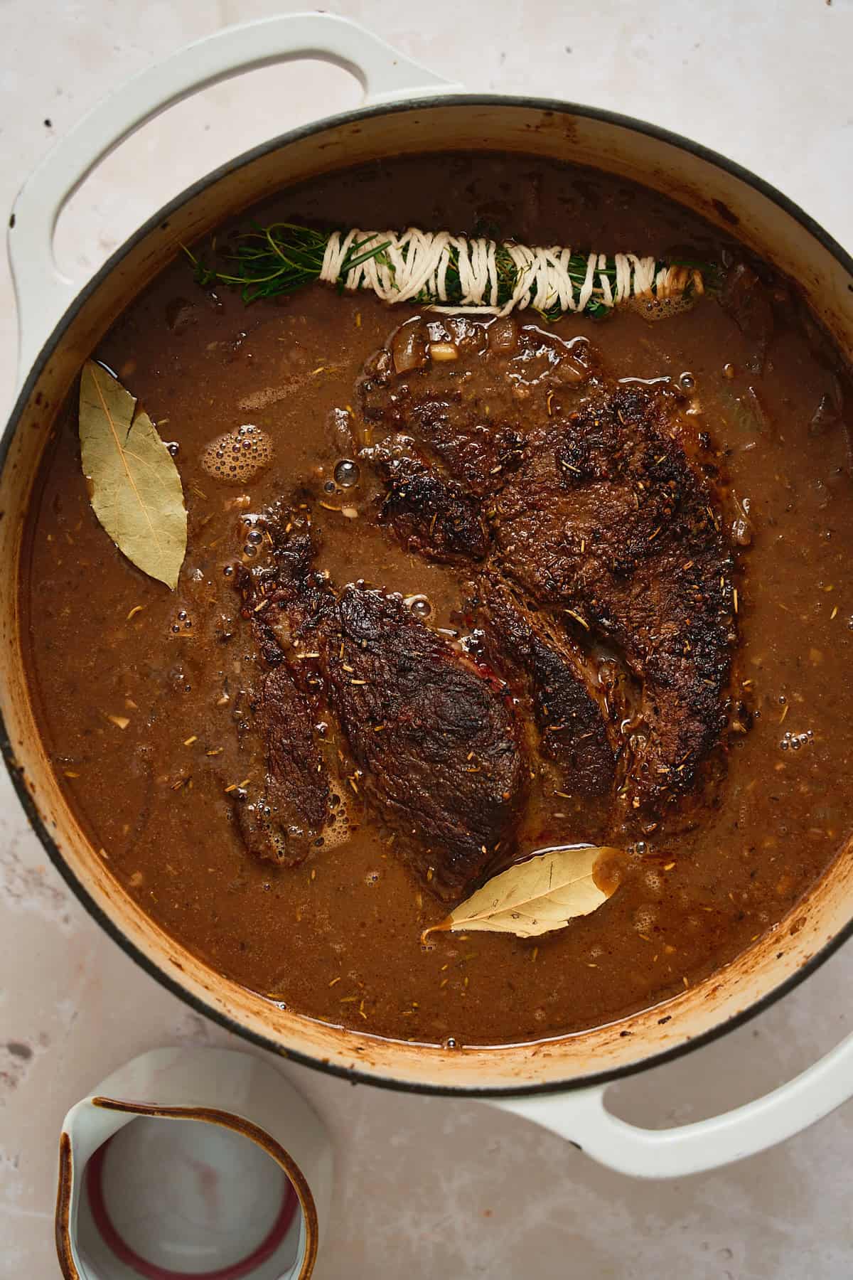 Browned beef chuck added to a Dutch oven with beef stock, bay leaves, and herbs added.