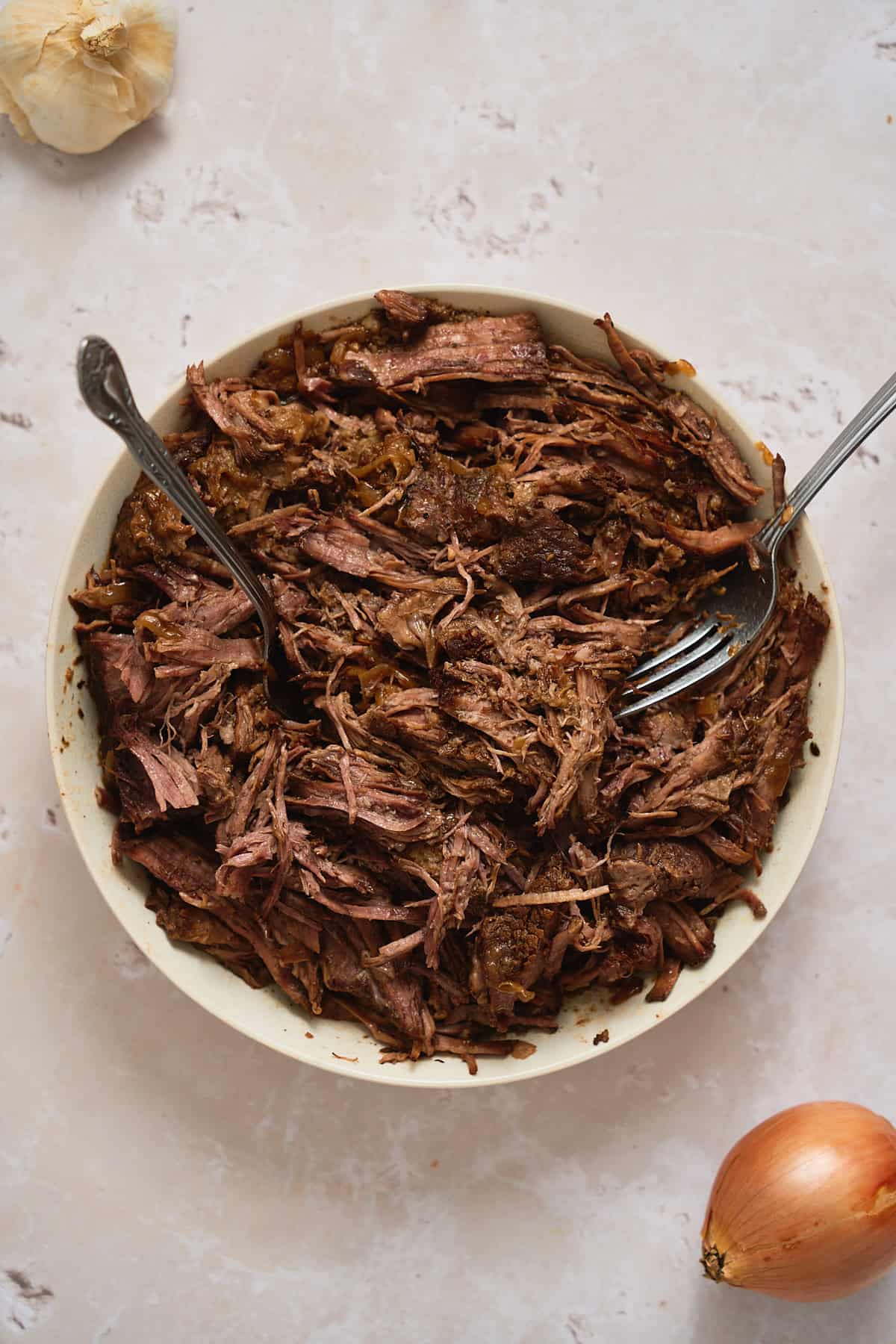 Shredded beef chuck roast in a bowl with two forks.