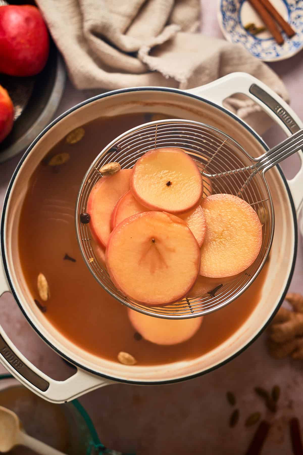 Apple slices after being mulled in apple cider being removed pot the pot with a metal skimmer.
