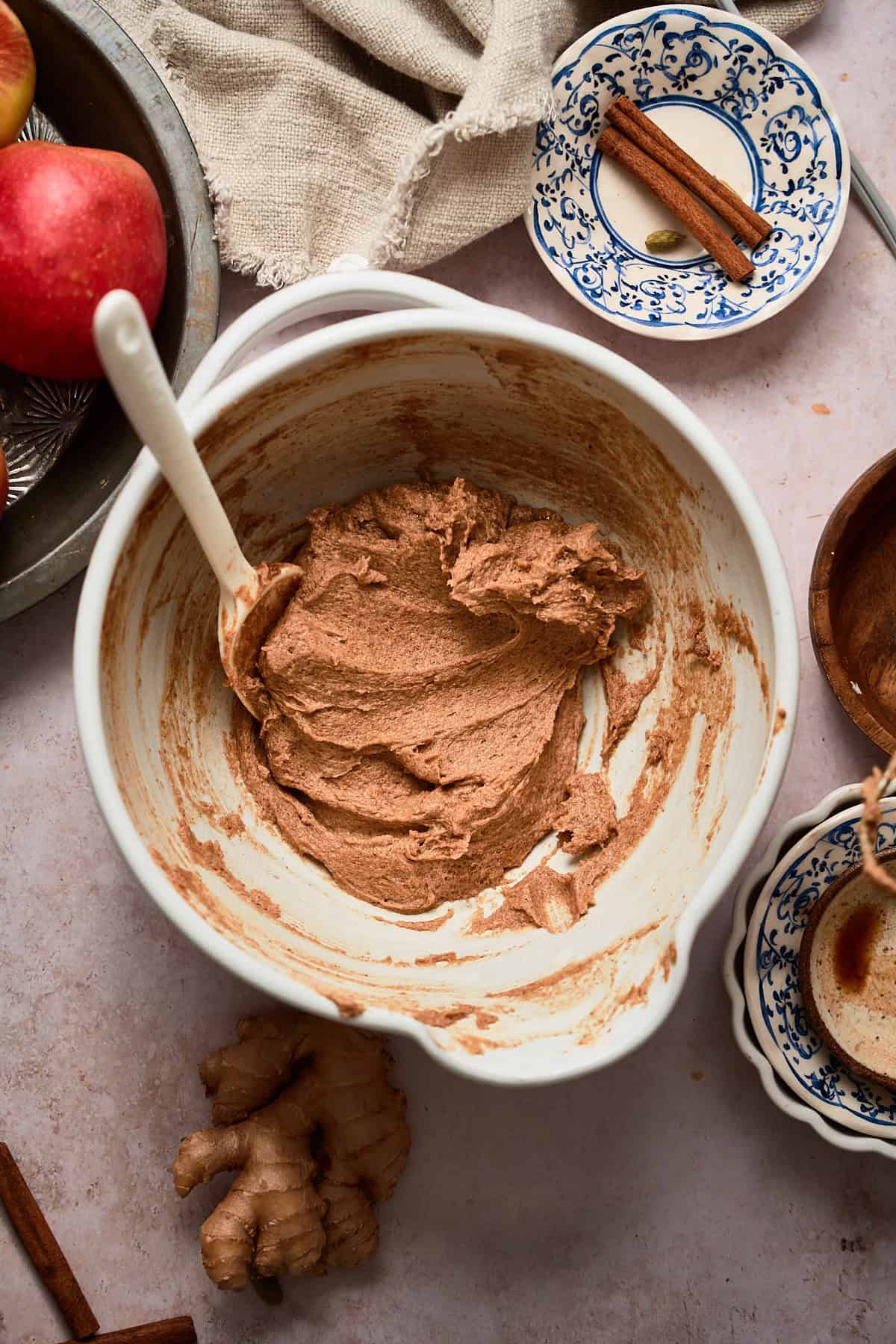 Softened and spiced butter in a bowl combined in a bowl with a rubber spatula surrounded by whole spices and apples.