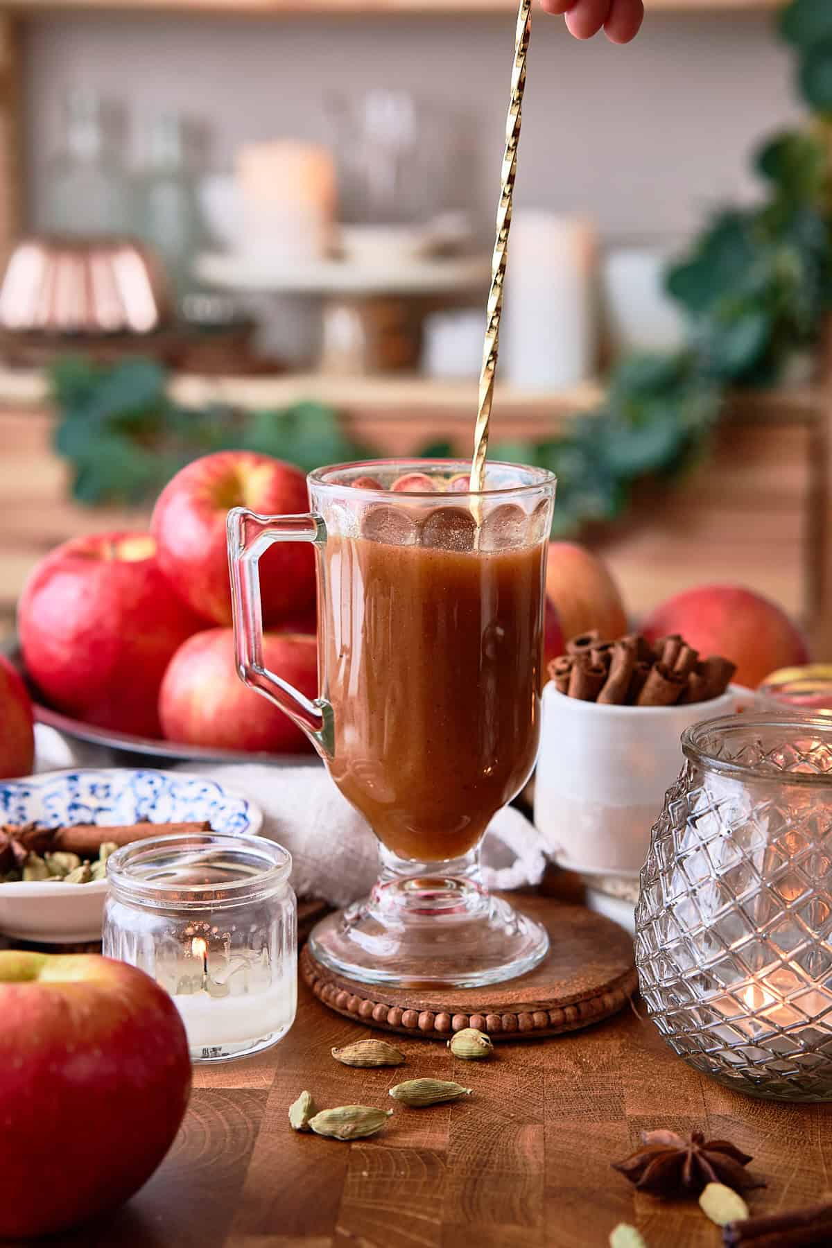 Hand stirring a golden spoon in a mug to dissolve butter and make an apple cider buttered rum.