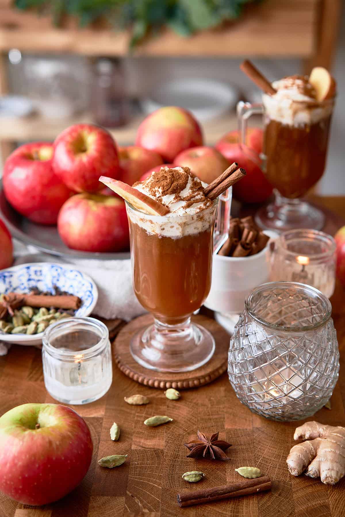 Rich apple cinnamon hot cocktail with whipped cream, cinnamon sticks, candles, and spices for cozy fall beverages.