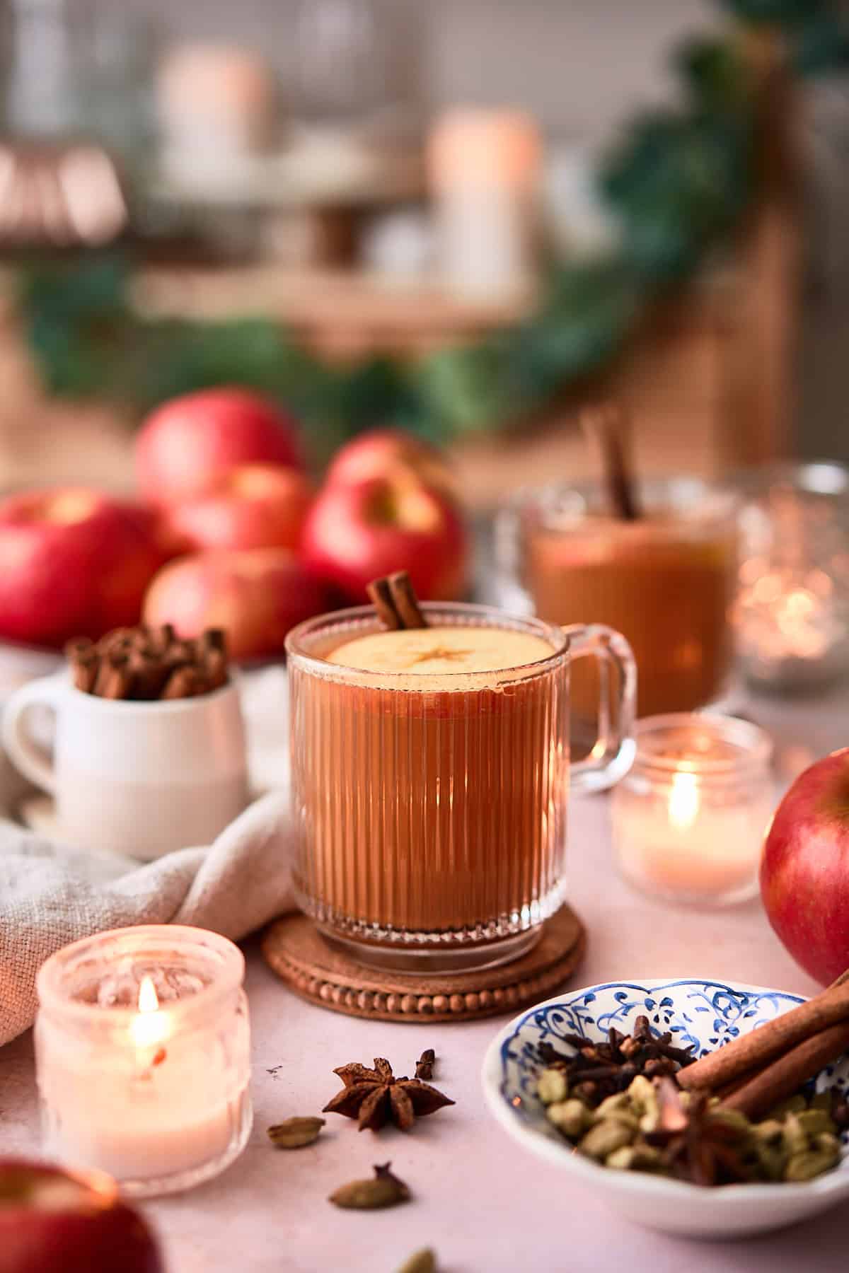 Cozy apple cinnamon spiced drinks for fall, surrounded by fresh apples and candles.