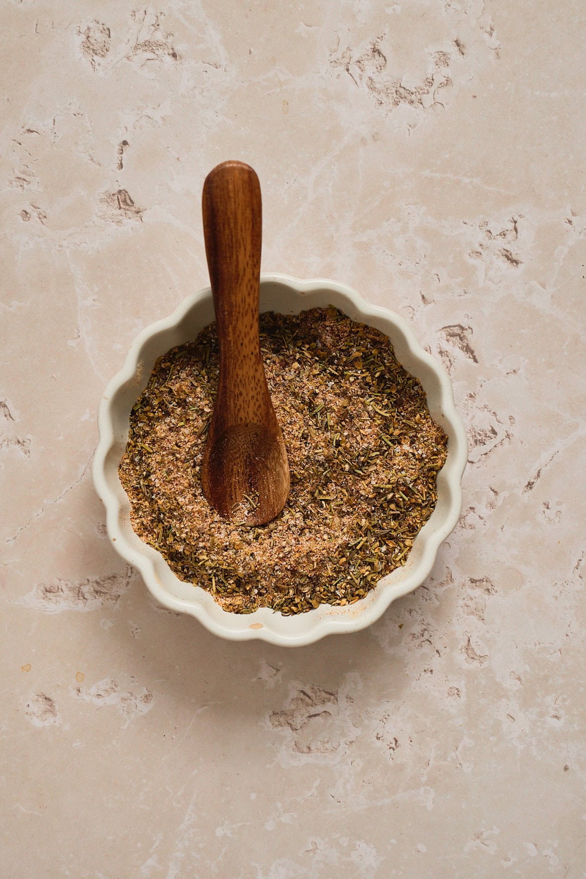 Dry seasoning rub in a ruffled white bowl with a small wooden spoon inside.
