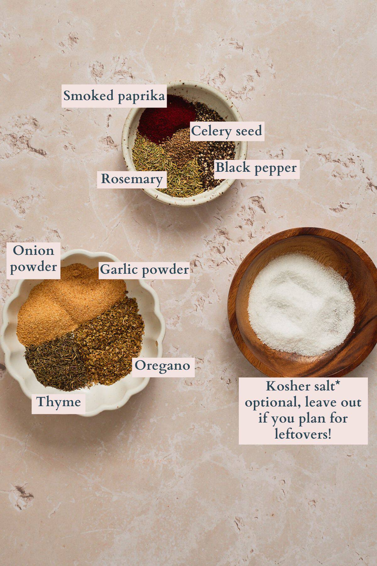 Dry spices and salt laid out in small bowls on a stone table, with each ingredient labeled to denote what it is.