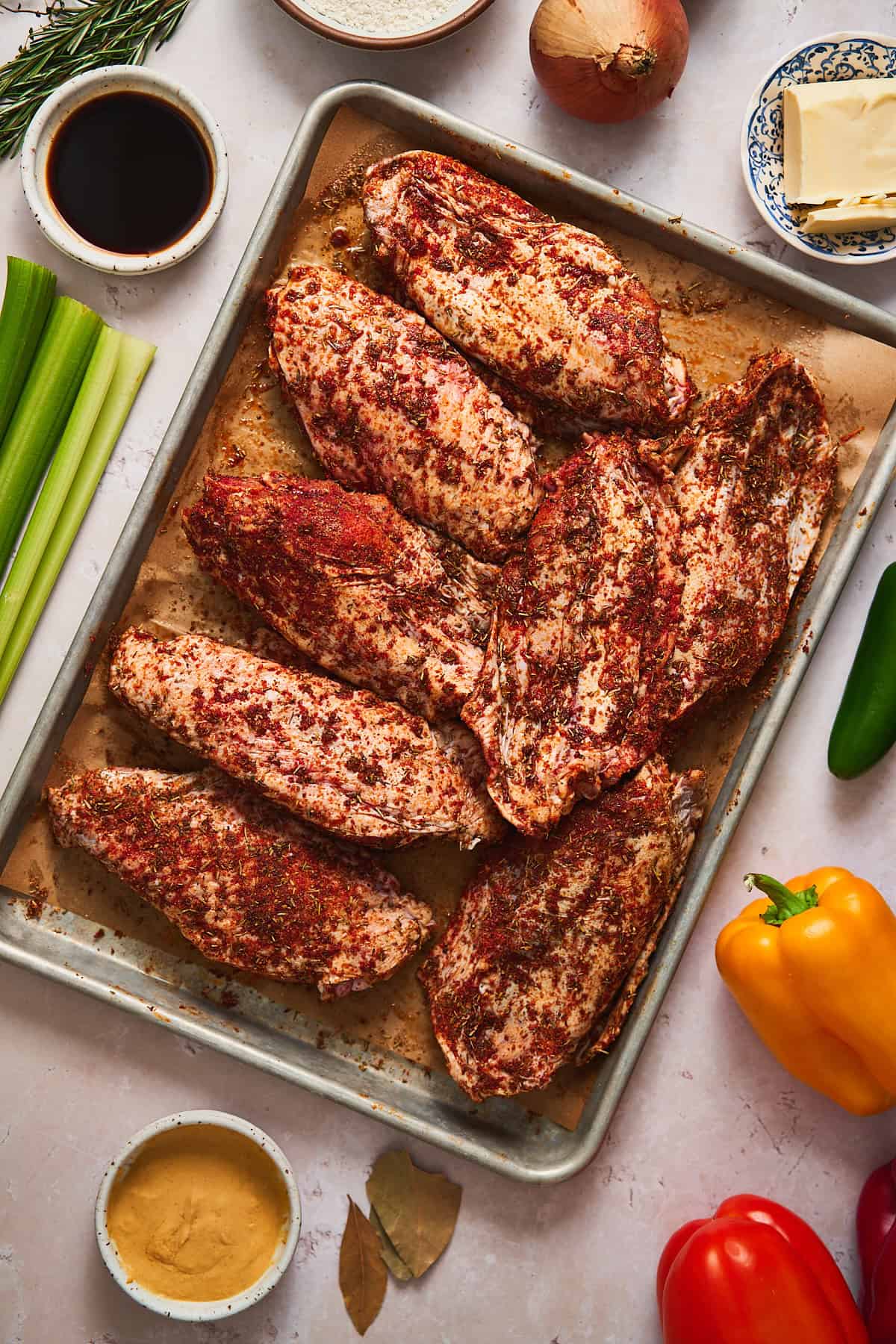 Seasoned turkey wings on a baking sheet, surrounded by bell peppers, onions, jalapenos, garlic, and more.