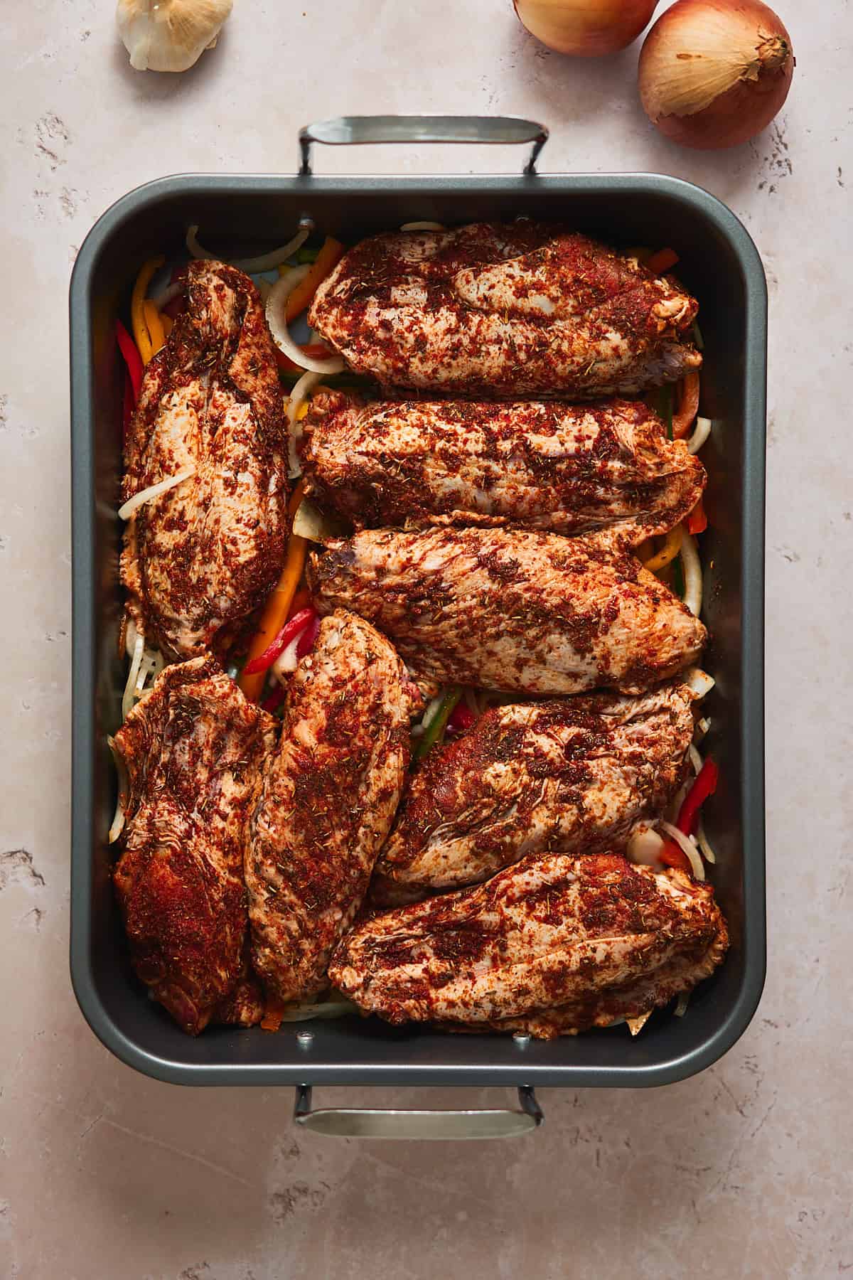 Raw well seasoned turkey wings in a roasting pan on top of bell peppers and onions.