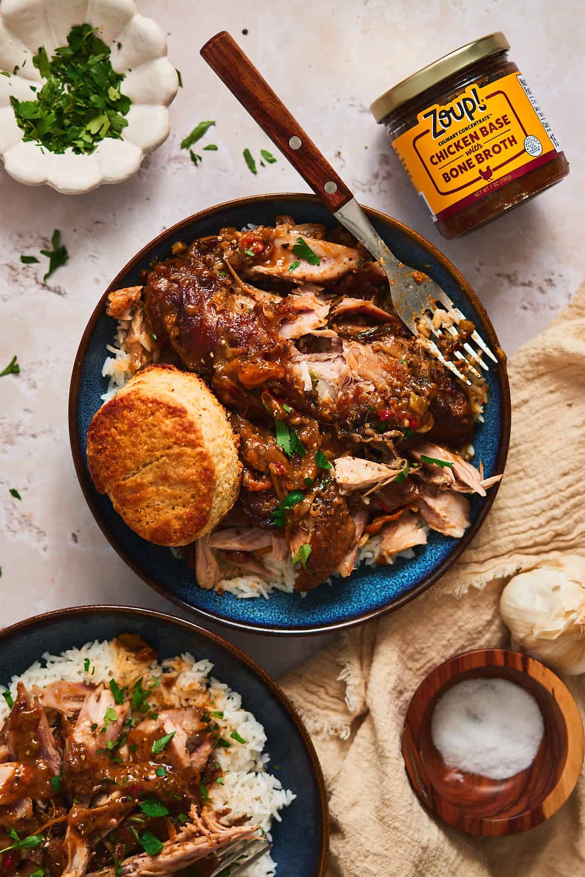 Shot of smothered turkey wings on a bed of rice in a blue bowl, surrounded by parsley, salt, a napkin, and another bowl.