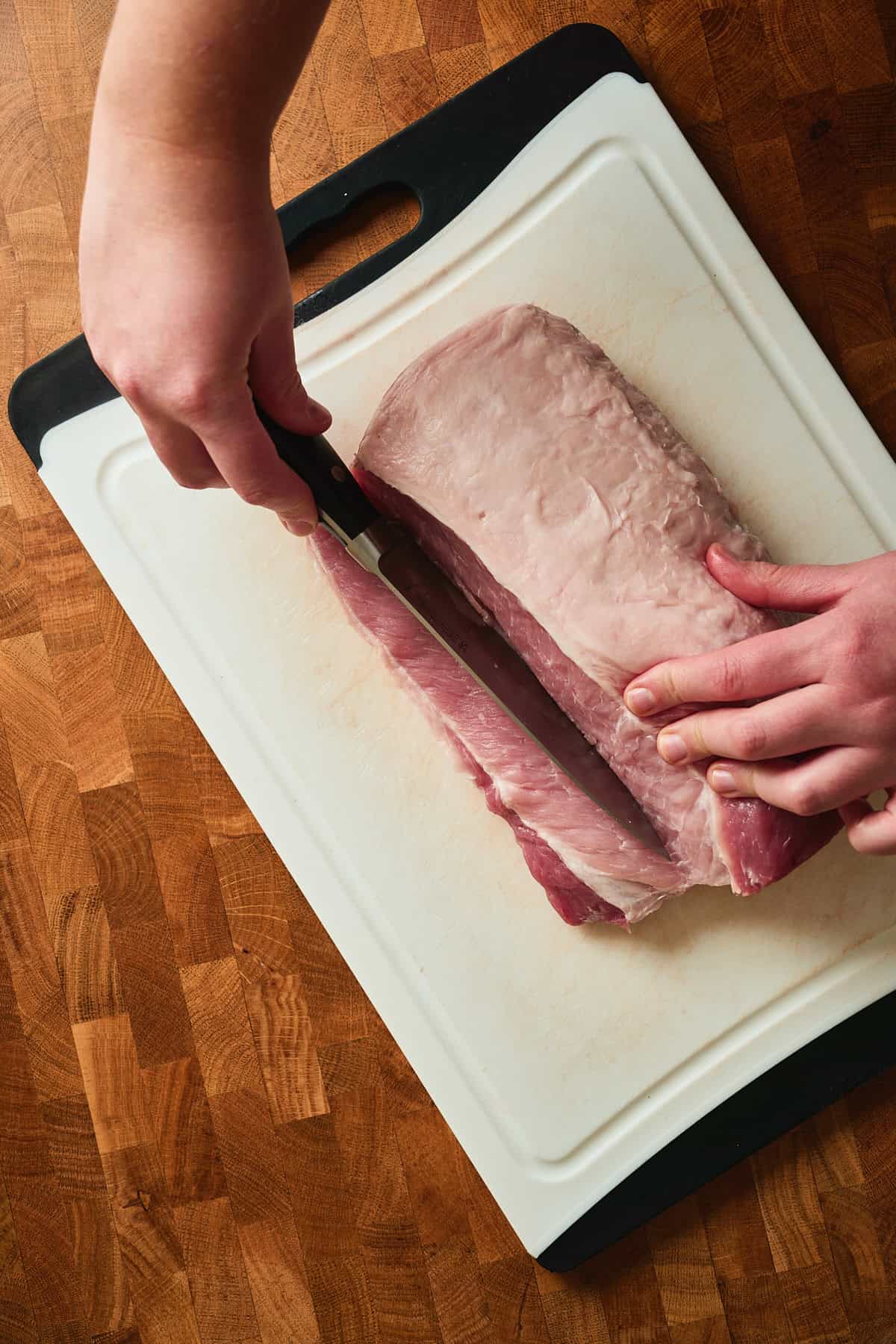 Raw pork loin being sliced on a cutting board.