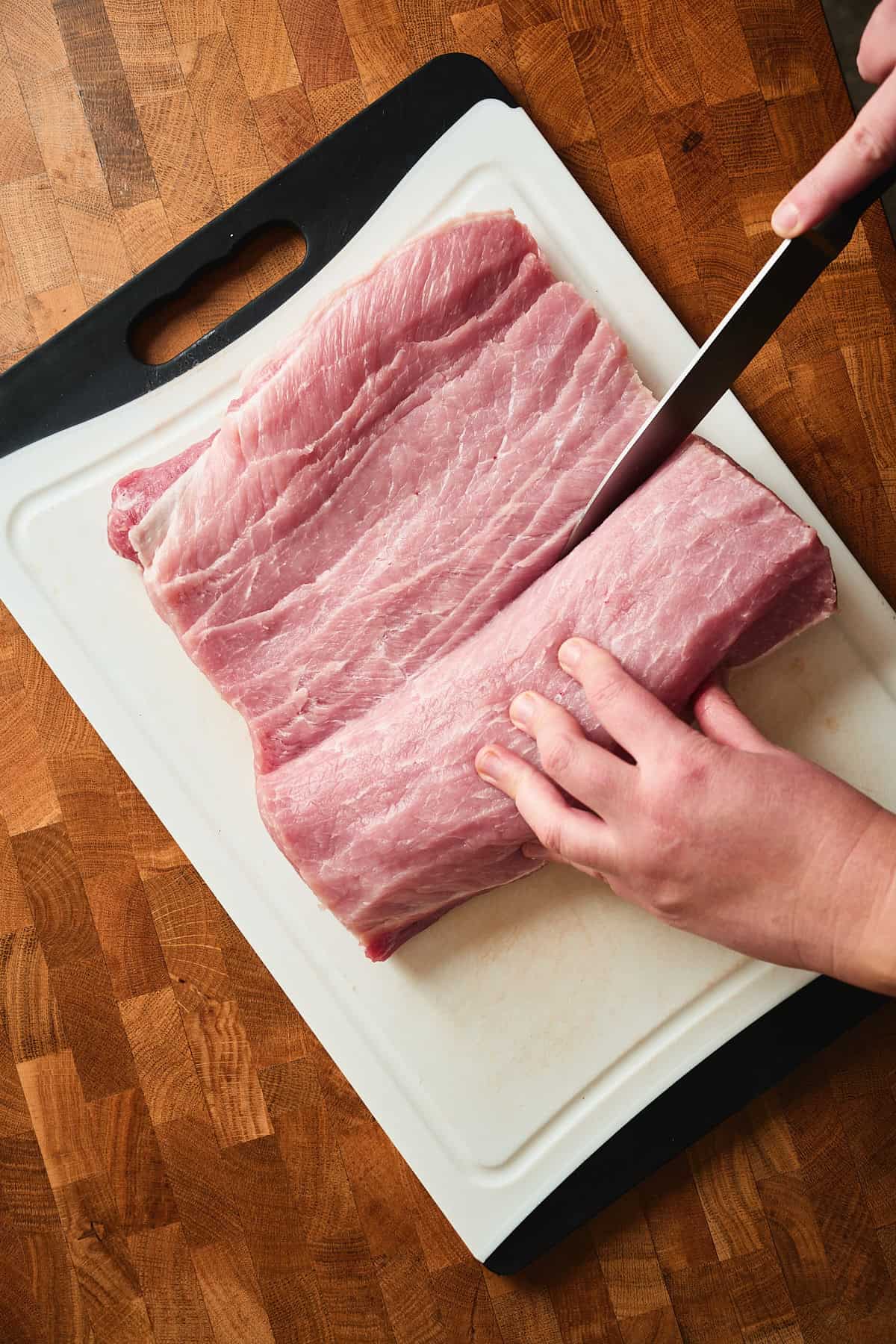 Fresh raw pork loin being butterflied on cutting board with knife.