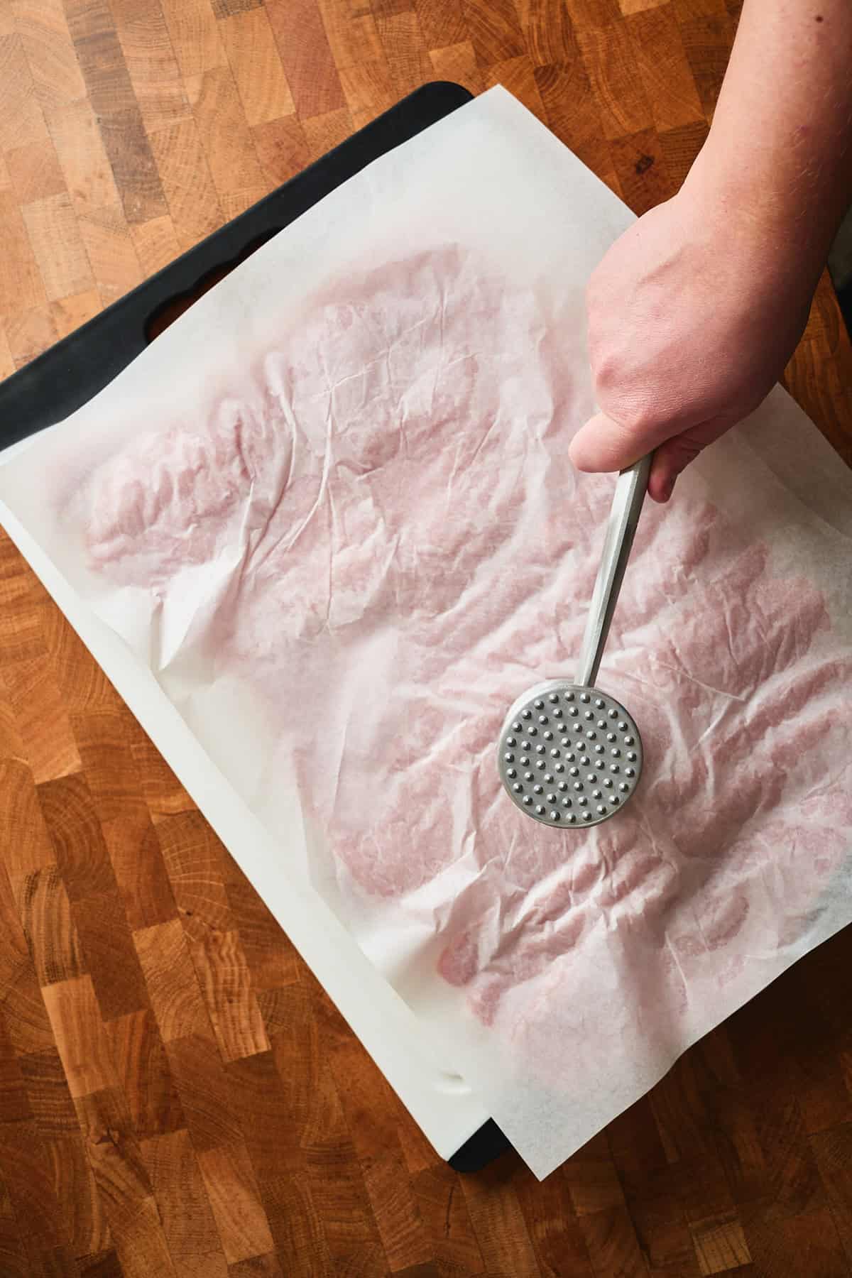 Hand pounding pork loin with a meat mallet.