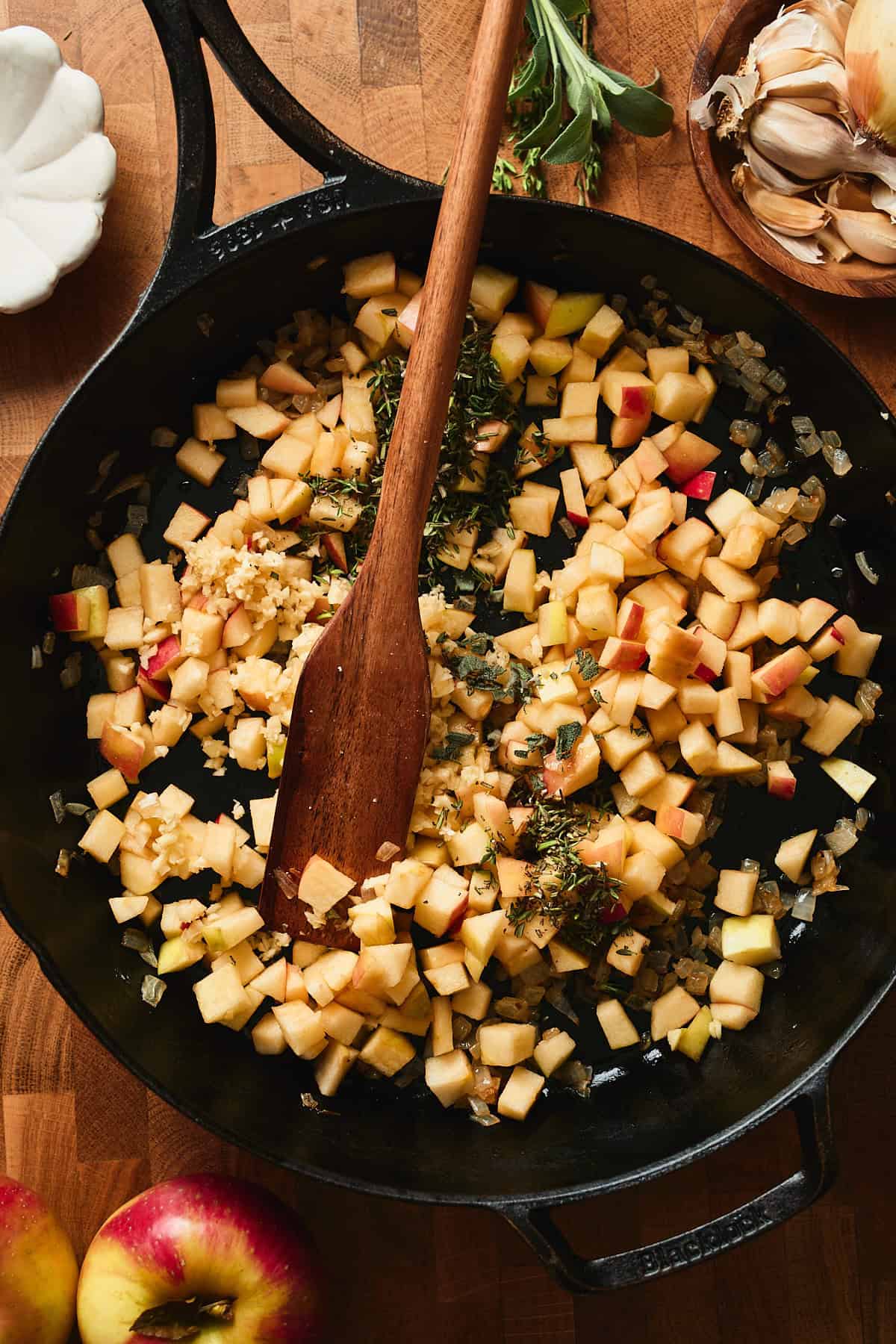Apples cooking in a skillet with onions, garlic, and herbs.