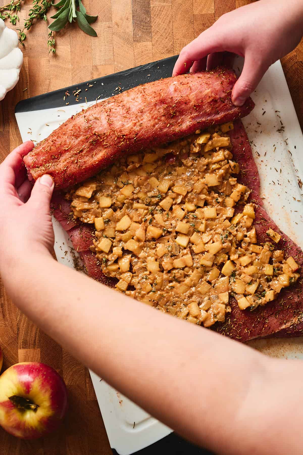 Hands rolling up a butterflied pork loin with an apple filling.