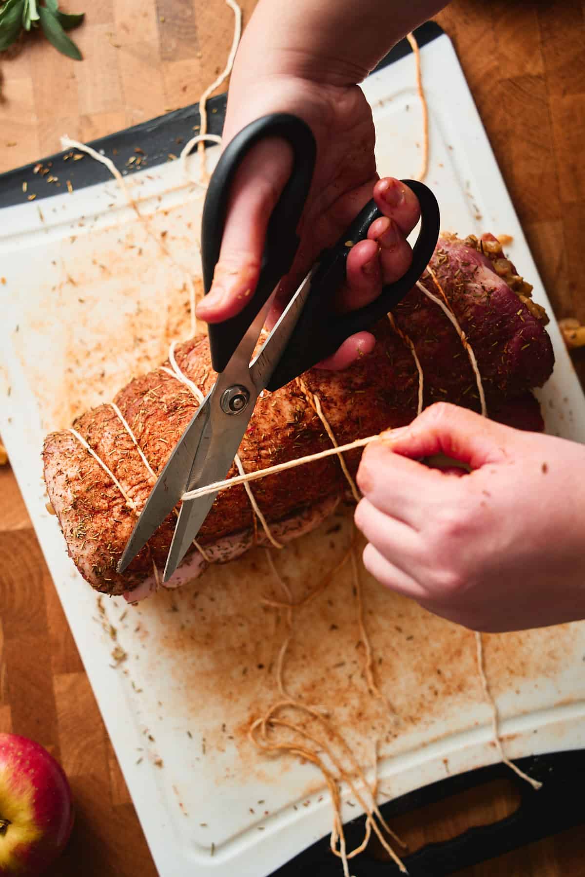 Hands cutting off excess kitchen twine on a rolled pork loin roast.
