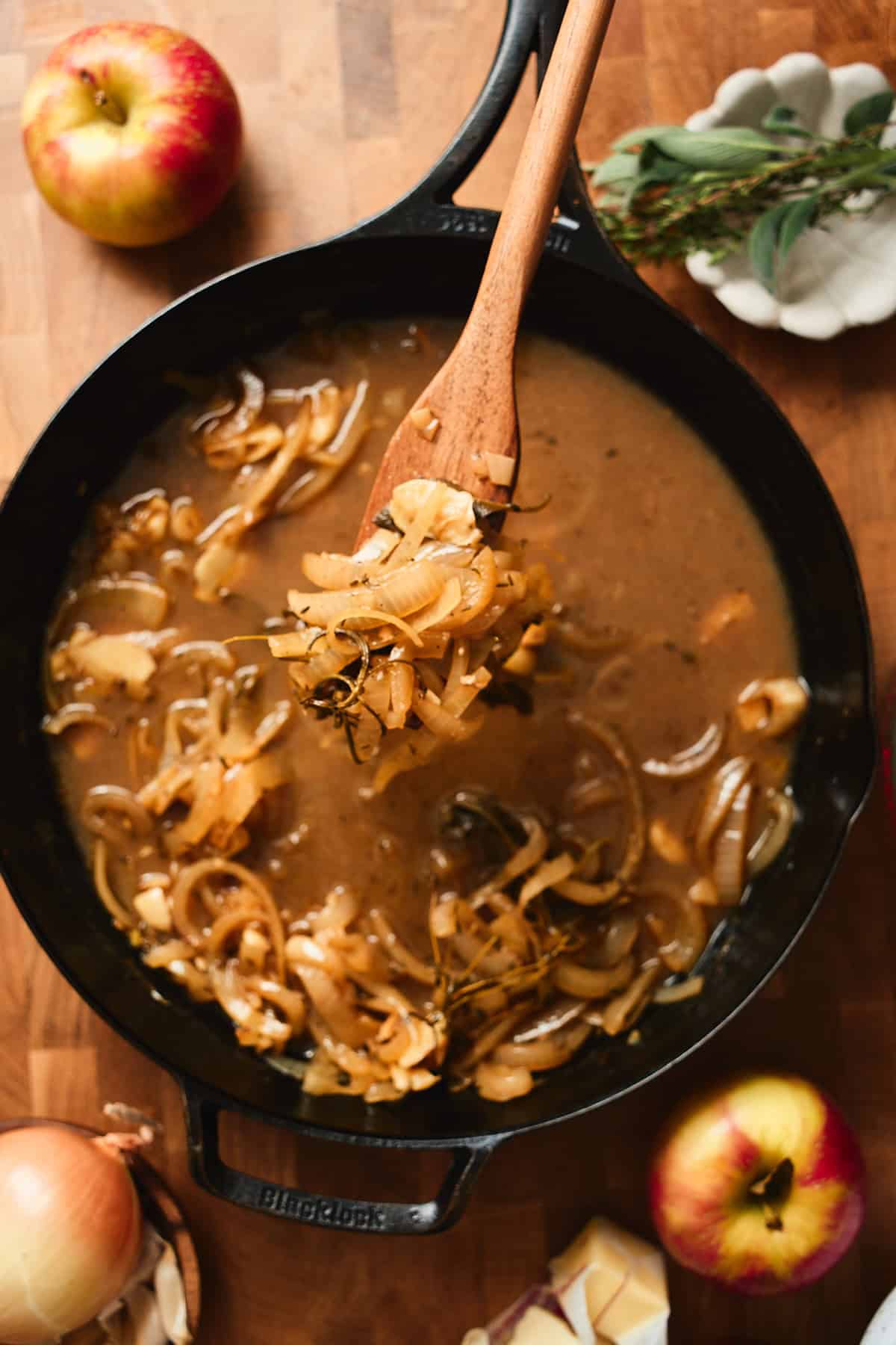Spoon holding cooked onions and garlic from a pan over a cast iron skillet.