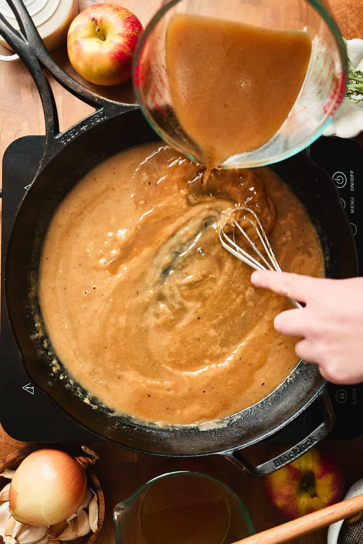 Hand whisking gravy in a pan while pouring in pan drippings.