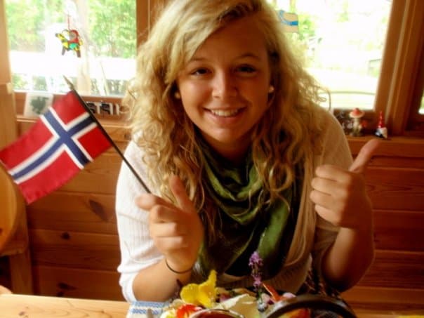 A woman holding a Norwegian flag wit ha thumbs up sitting in front of a plate of food.
