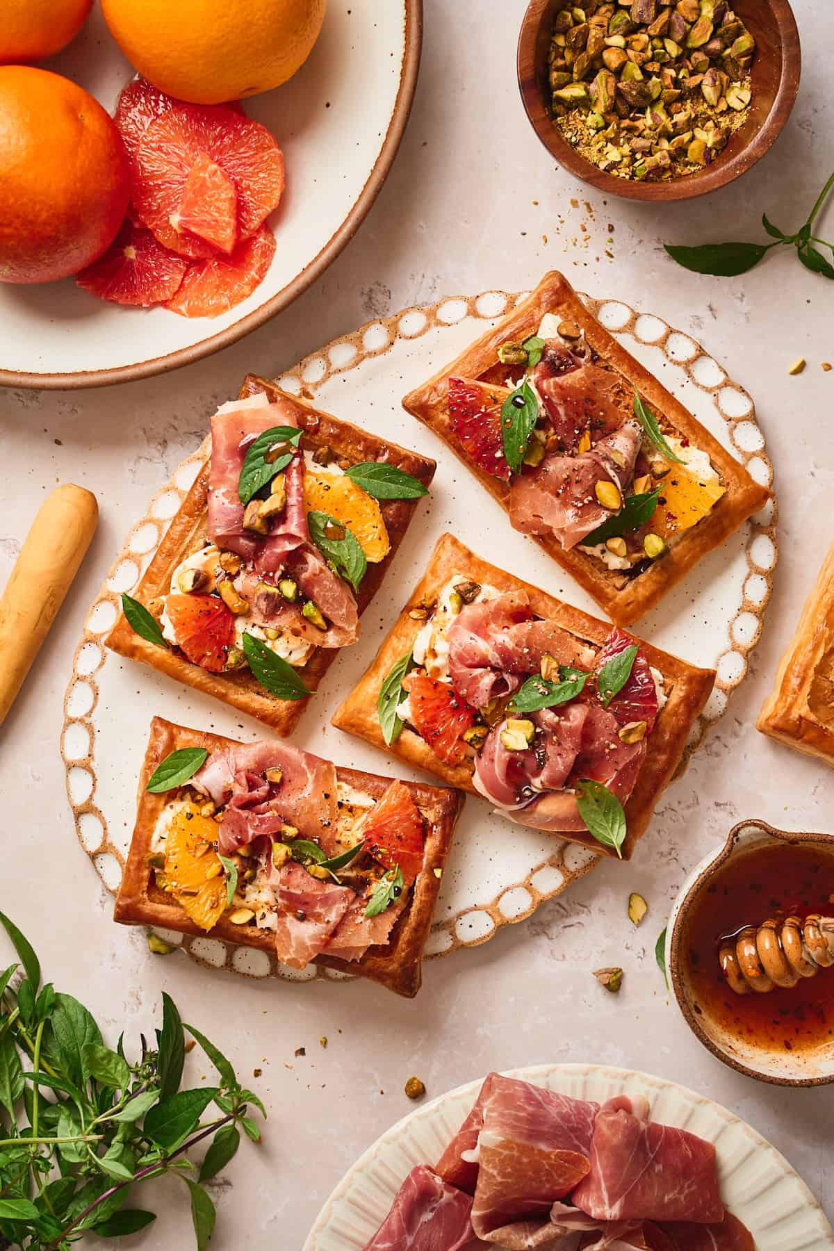 Overhead view of a ceramic tray full of burrata and prosciutto tarts topped with fresh citrus, basil, and honey.