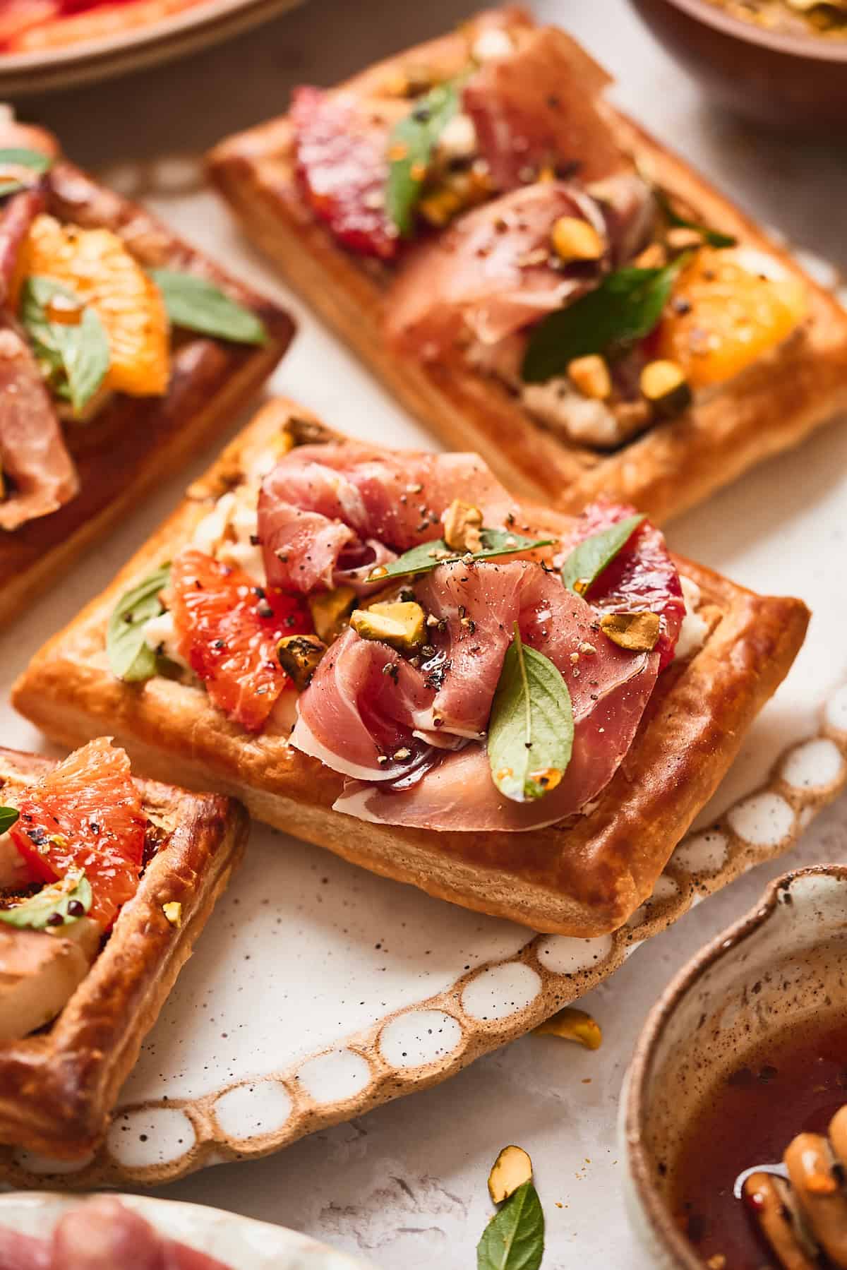 Beautiful puff pastry tart topped with burrata, prosciutto, basil, orange segments, and pistachios.