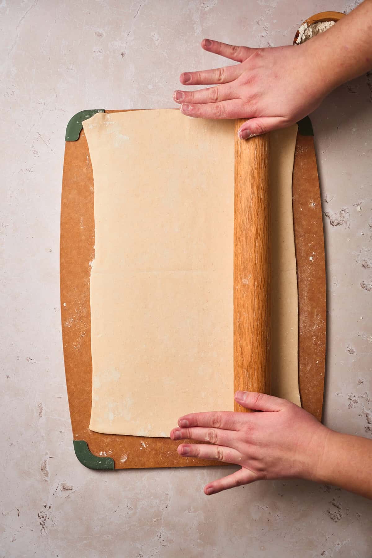 Hands using a rolling pin to flatten puff pastry.