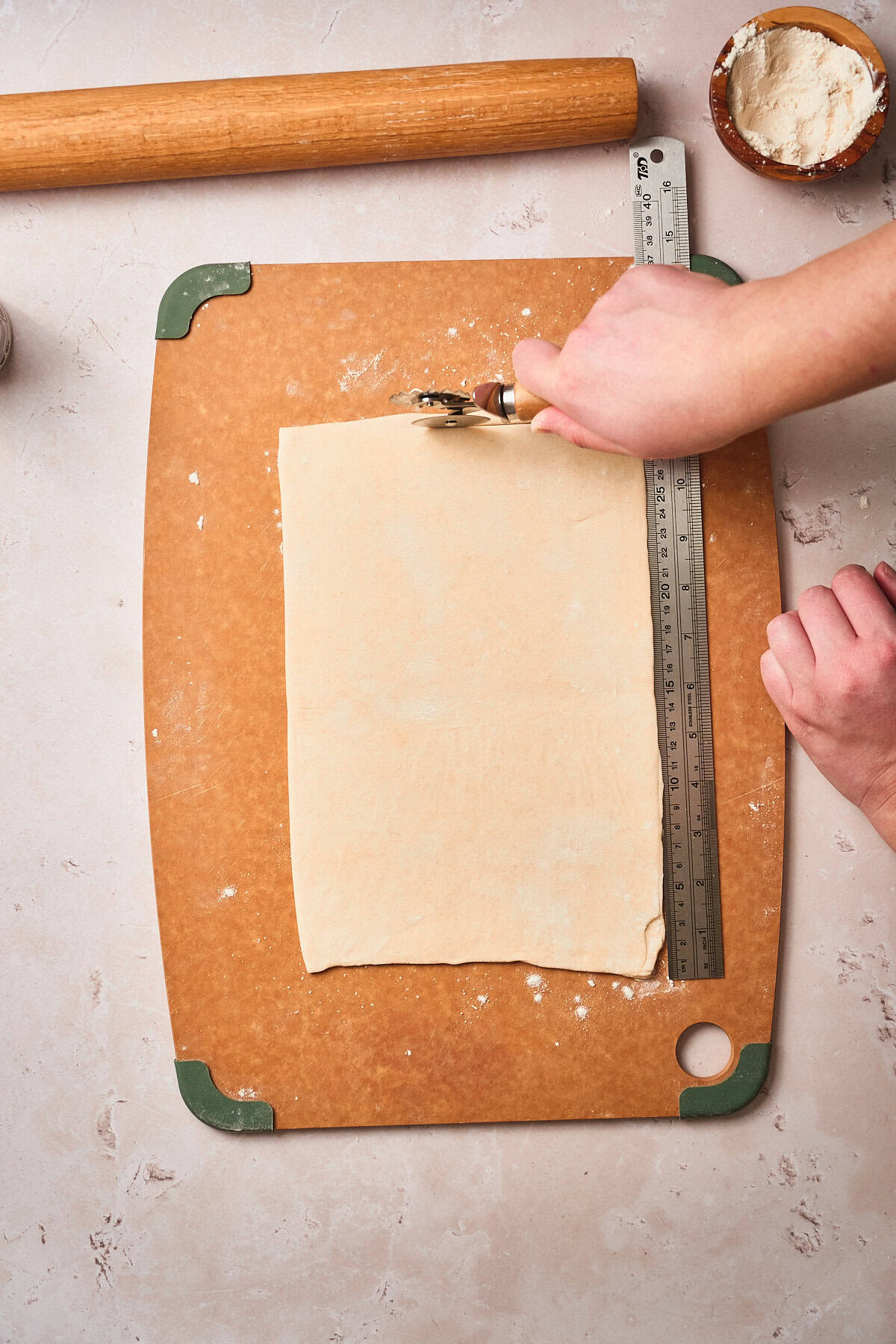 Hands trimming edges with a pastry wheel for a cleaner rectangle shape.