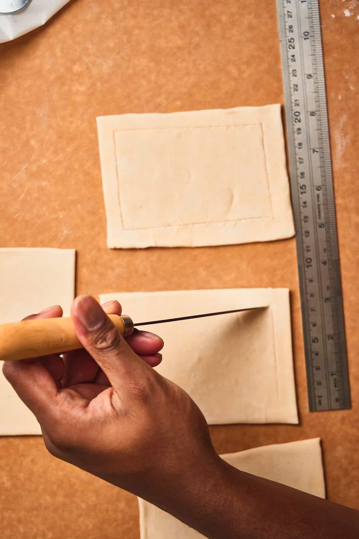 Hand scoring the edge of a puff pastry square with a sharp knife.
