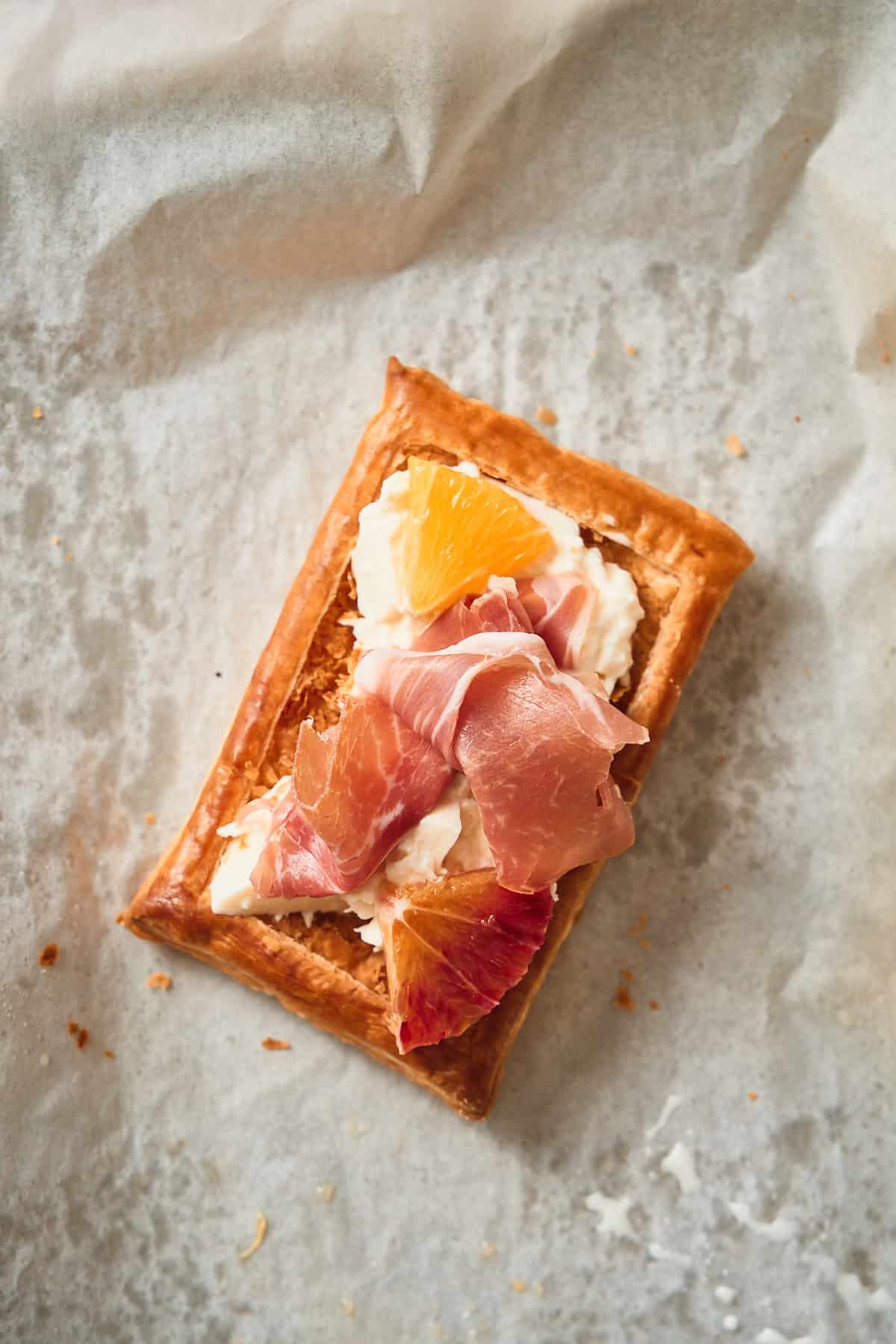 Golden brown puff pastry topped with burrata followed by prosciutto and orange segments.