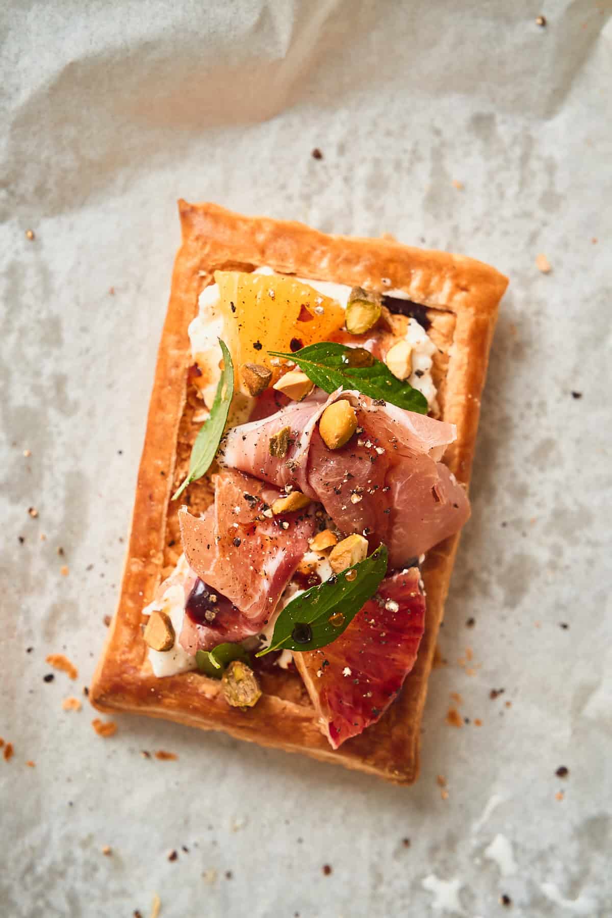 super beautiful puff pastry topped with burrata, citrus, prosciutto, basil, pistachio, and hot honey.