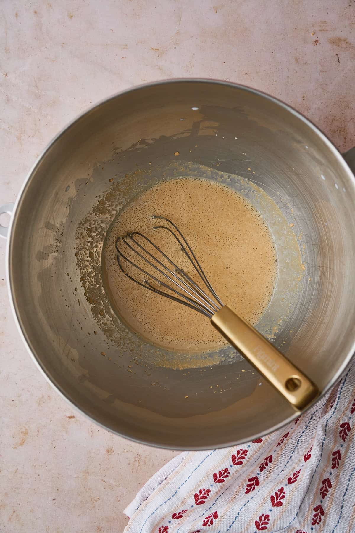 Foamy yeast in a mixing bowl with a whisk.