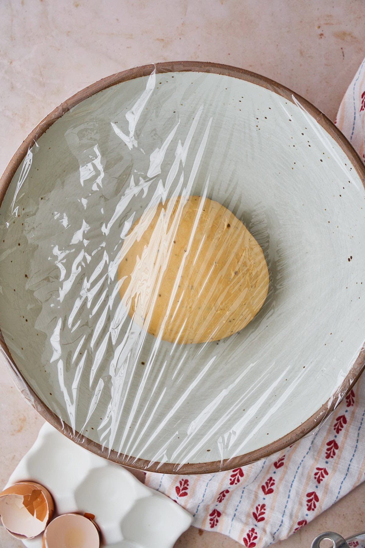 Bowl of dough in a large bowl covered with plastic wrap.