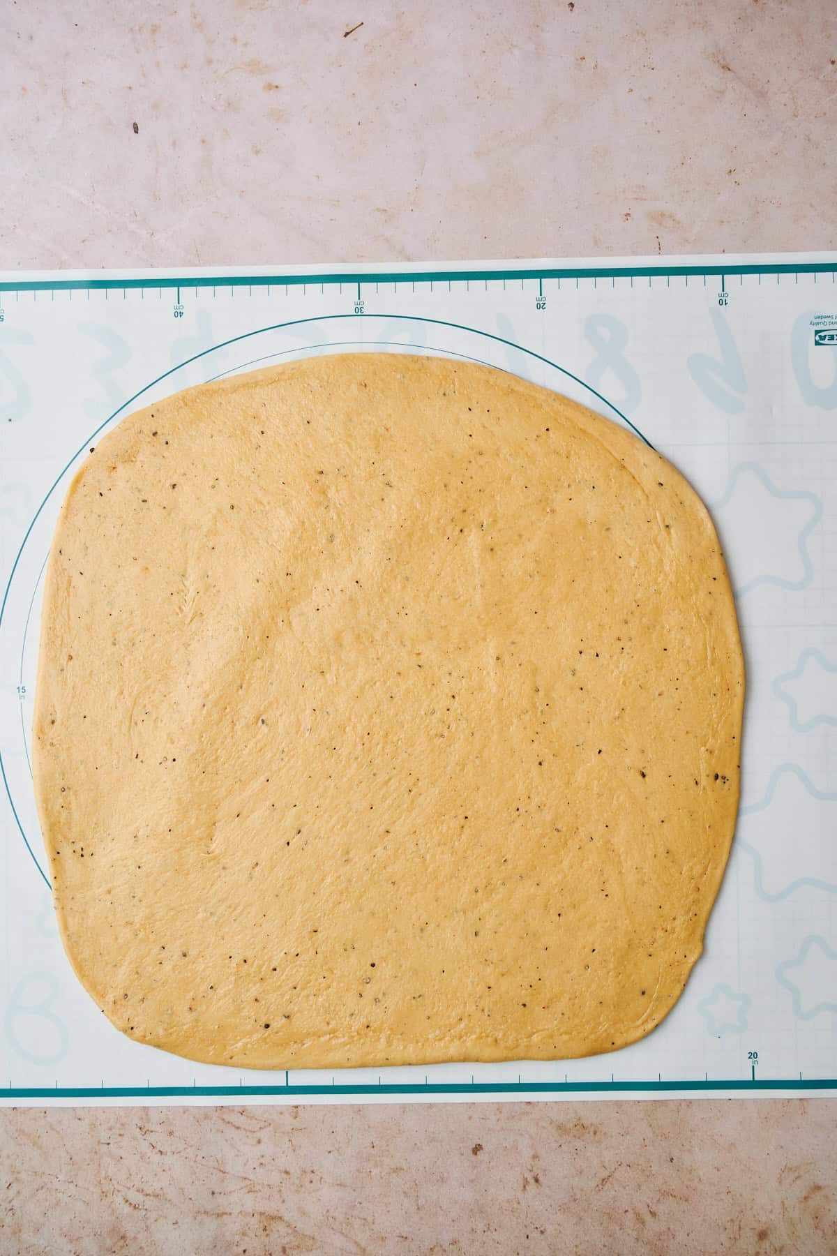 Cardamom bun dough on a silicone baking mat rolled flat.