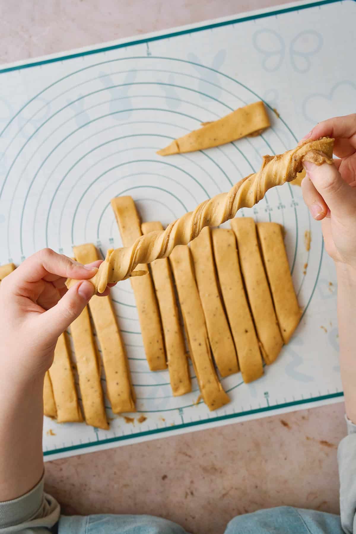 Hands twisting strips of dough to create a knot shape.