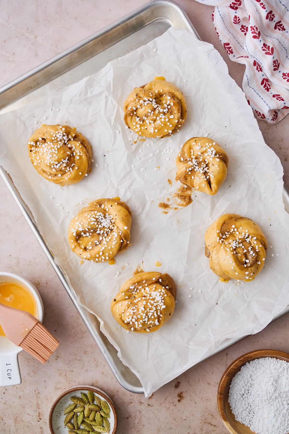 Buns brushed with egg wash, and topped with pearl sugar on a parchment lined baking sheet.