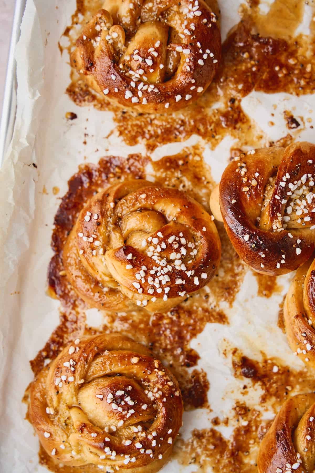 Freshly baked cardamom buns on a parchment lined baking sheet.